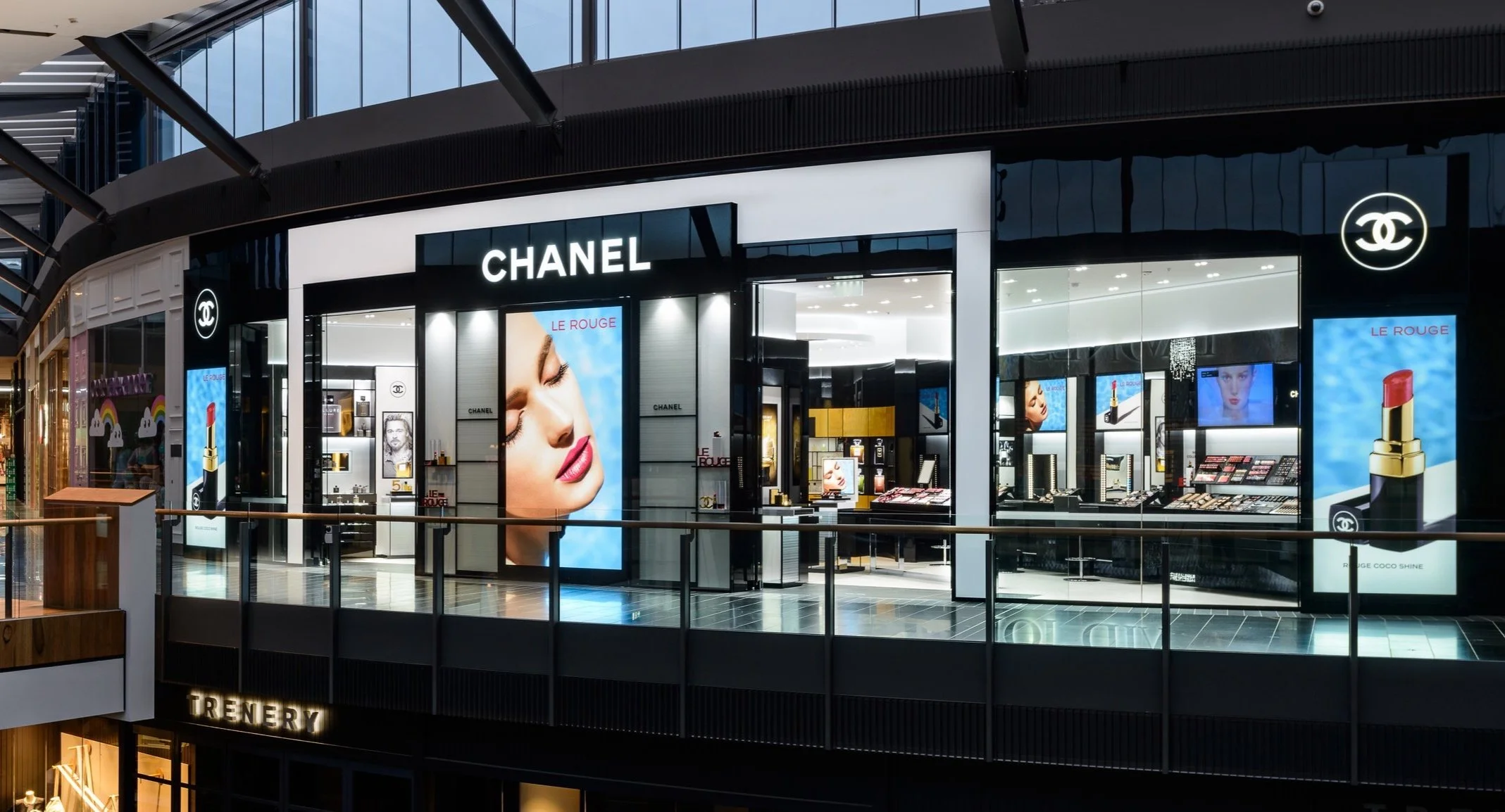 Exterior view of a Chanel cosmetics store on a mall second floor, featuring digital advertisements and the Chanel logo.