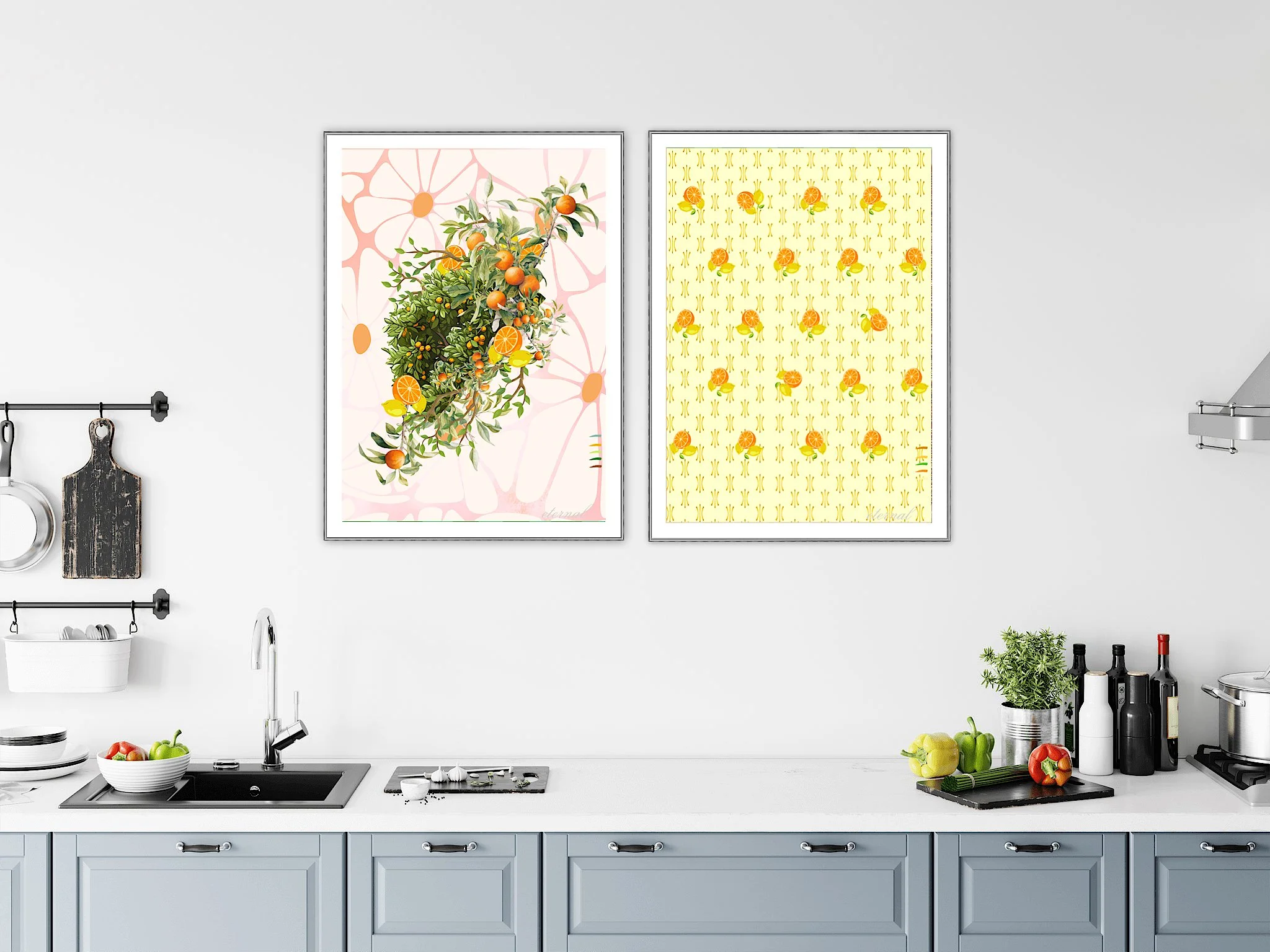 Two framed pictures of oranges hanging on a white wall in a kitchen. The left picture shows a bunch of oranges on a branch, the right picture has a yellow background with orange slices and small motifs.