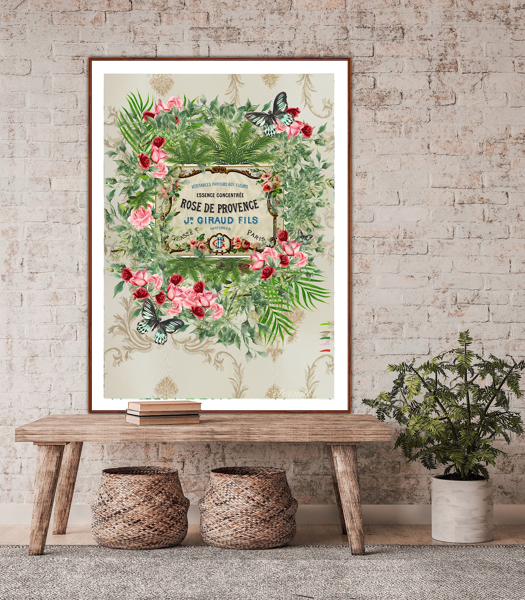 Decorative framed poster with a floral and butterfly design, featuring text about rose perfume, on a brick wall behind a wooden table with books and woven baskets, and a potted plant nearby.