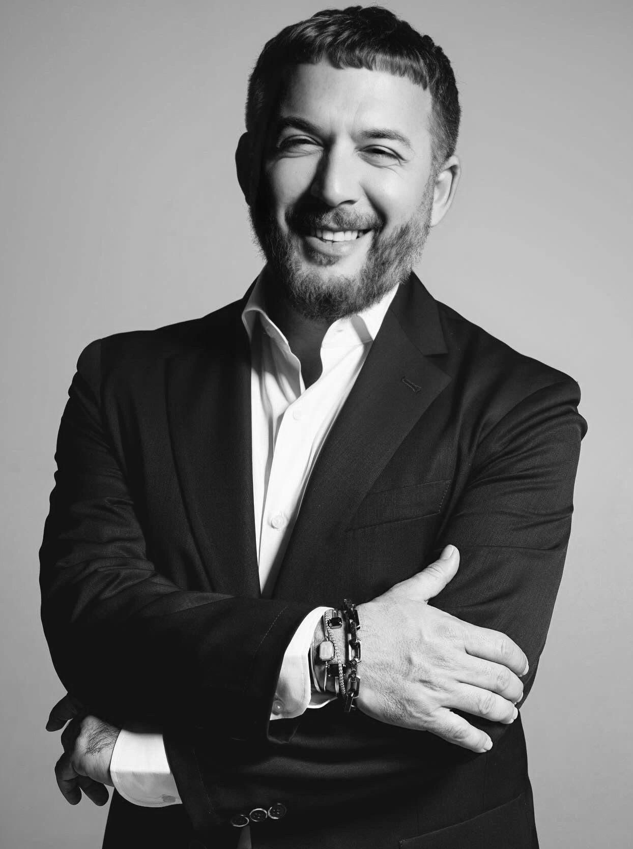 Black and white portrait of a smiling man in a suit crossing his arms.