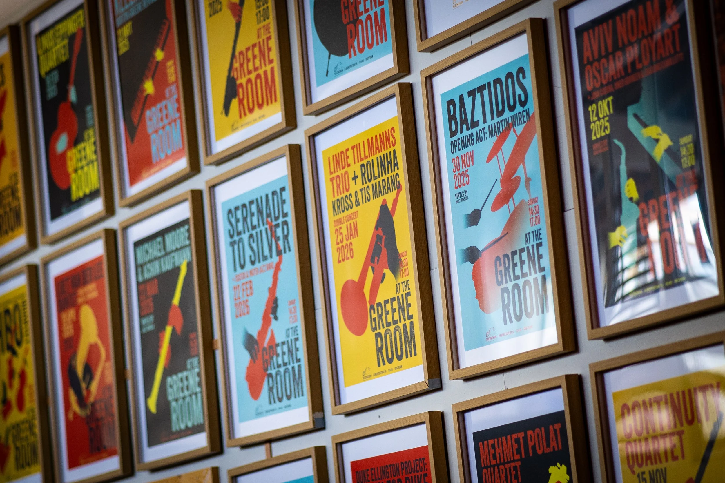 Wall decorated with numerous framed vibrant posters for various art and music events, featuring bold text and graphics.