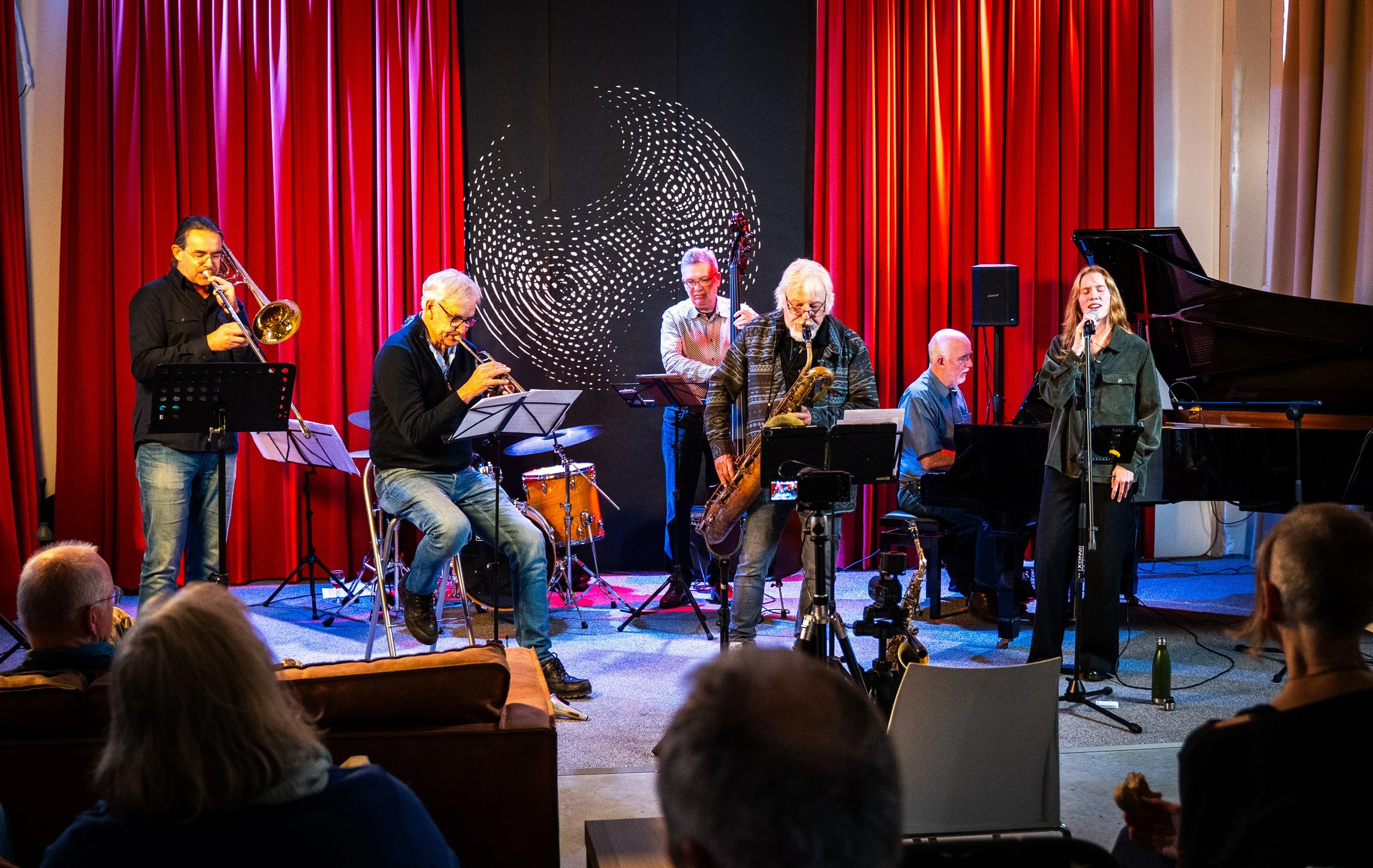 A jazz band performing on stage with audience members in the foreground.
