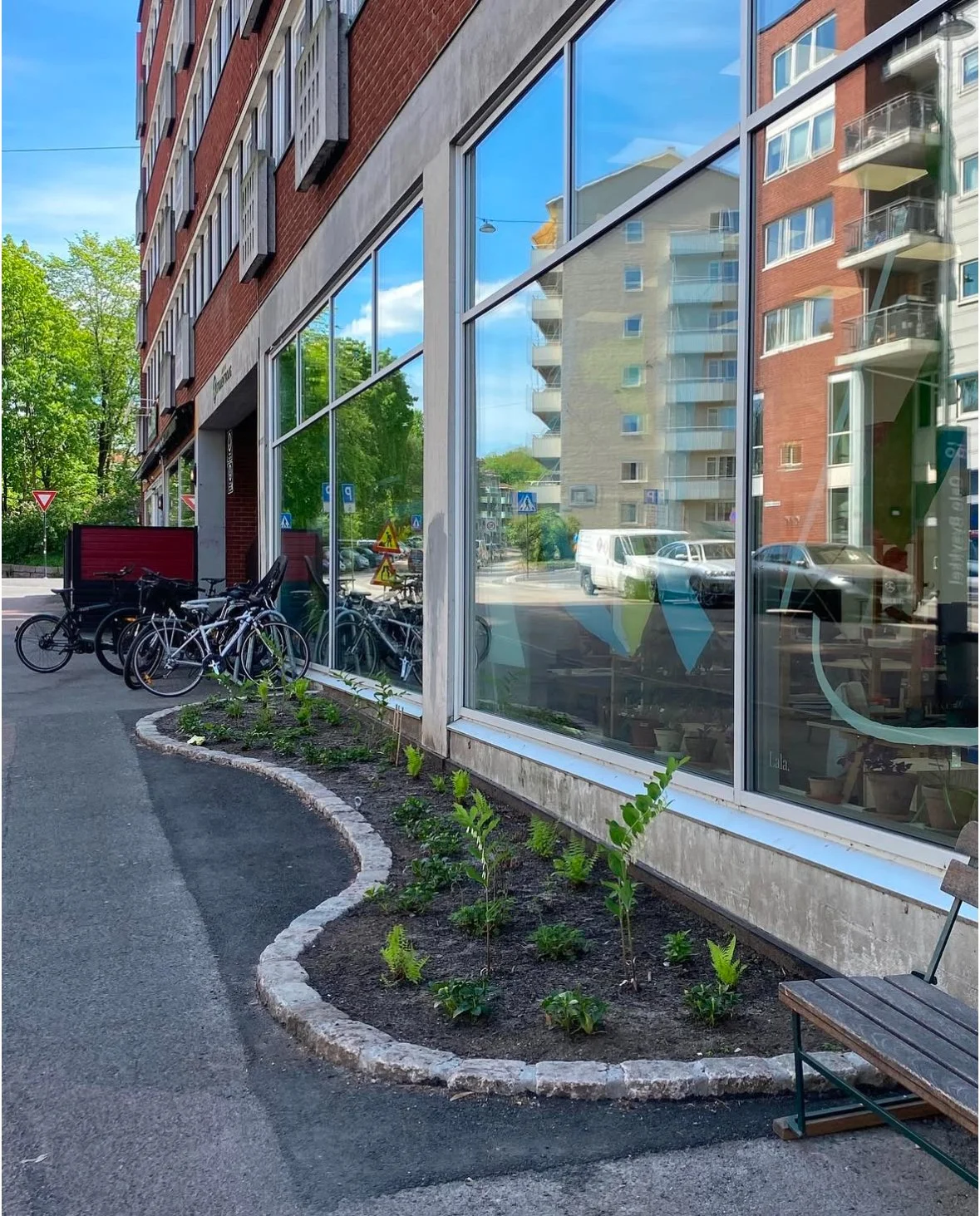 Sidewalk with bike rack and small garden outside building with large windows