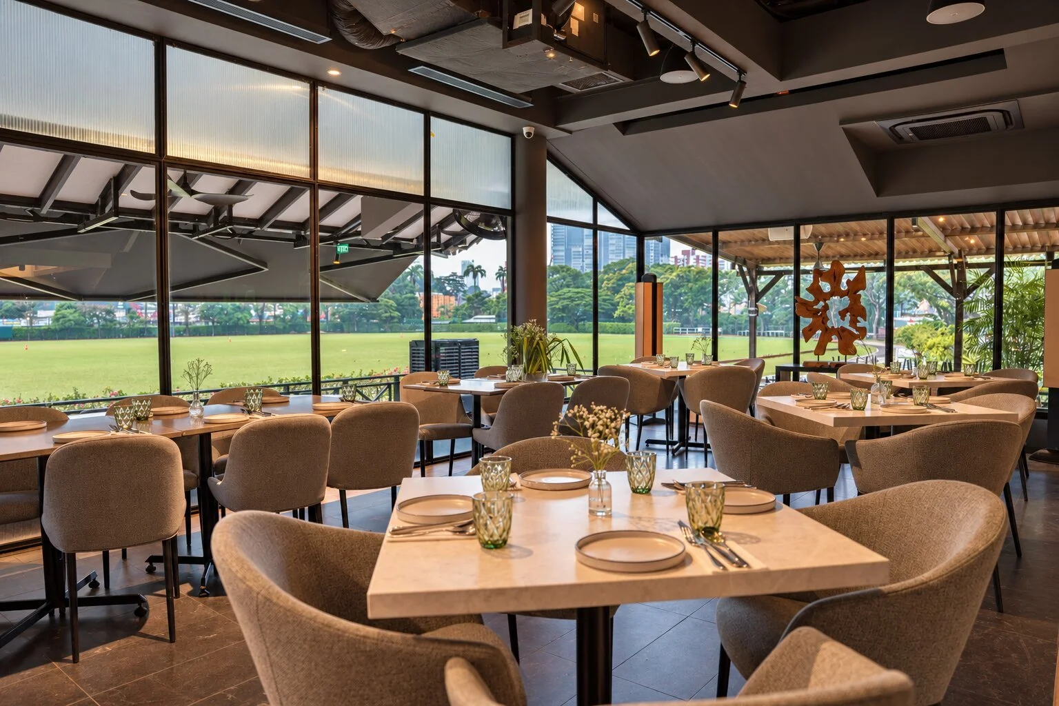 Elegant event setup in a modern venue with large windows, string lights, and floral arrangements on tables for a celebration or wedding reception.