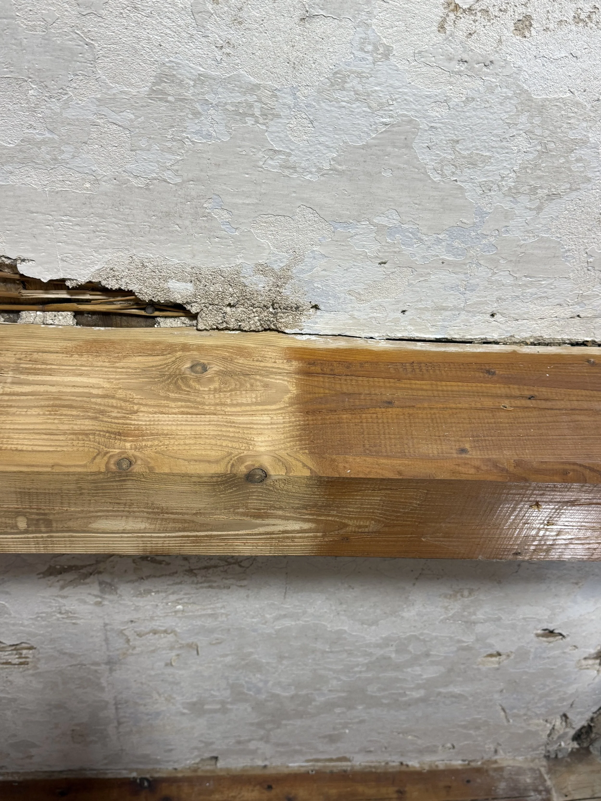 Ein Wandabschnitt mit abblätternder Farbe und sichtbarem Holzboden, die Wand zeigt Verschleiß und Alterung.