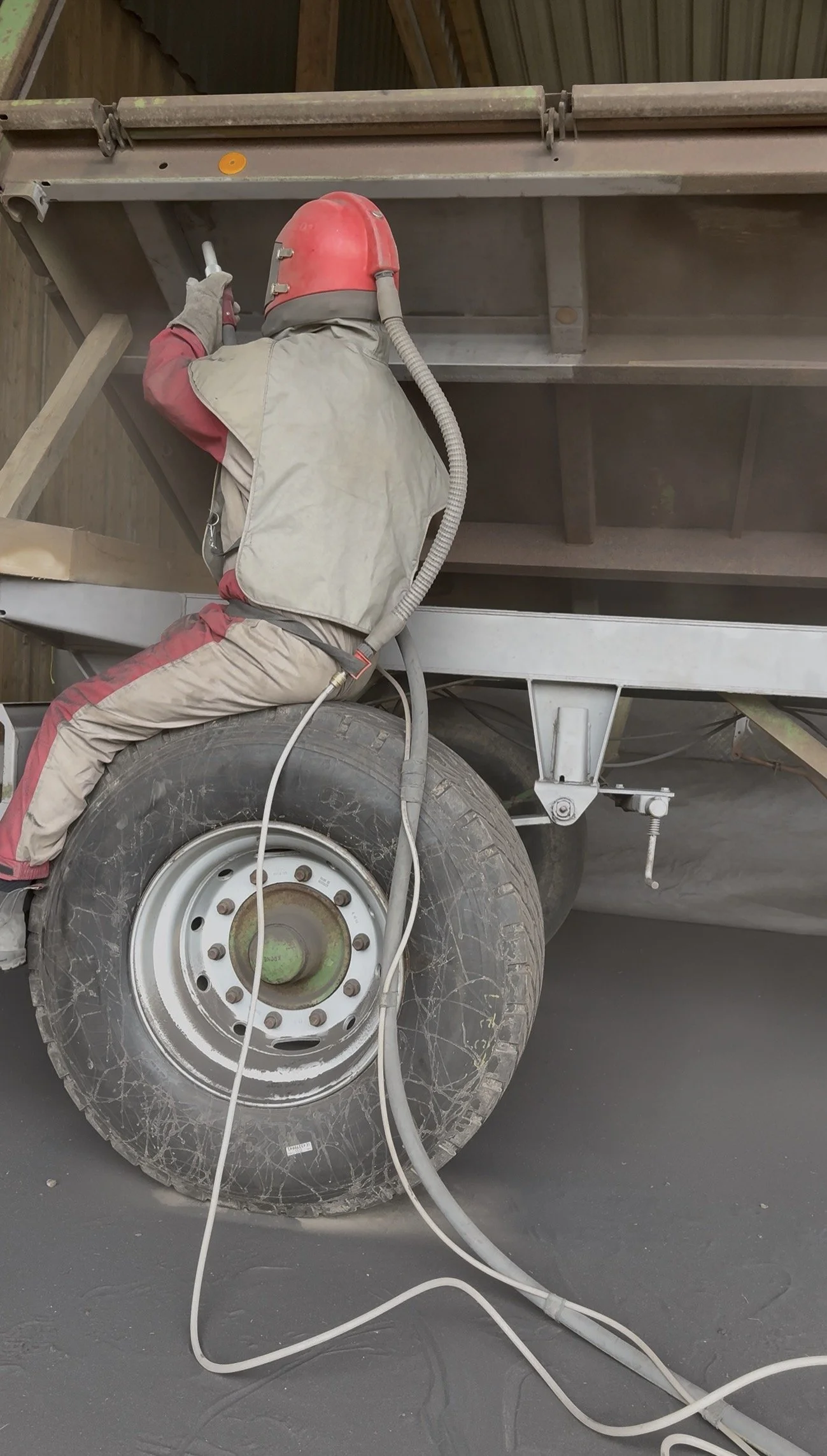 Arbeiter in Schutzkleidung und Helm arbeitet an einem großen, staubigen Anhänger und verwendet ein Werkzeug.