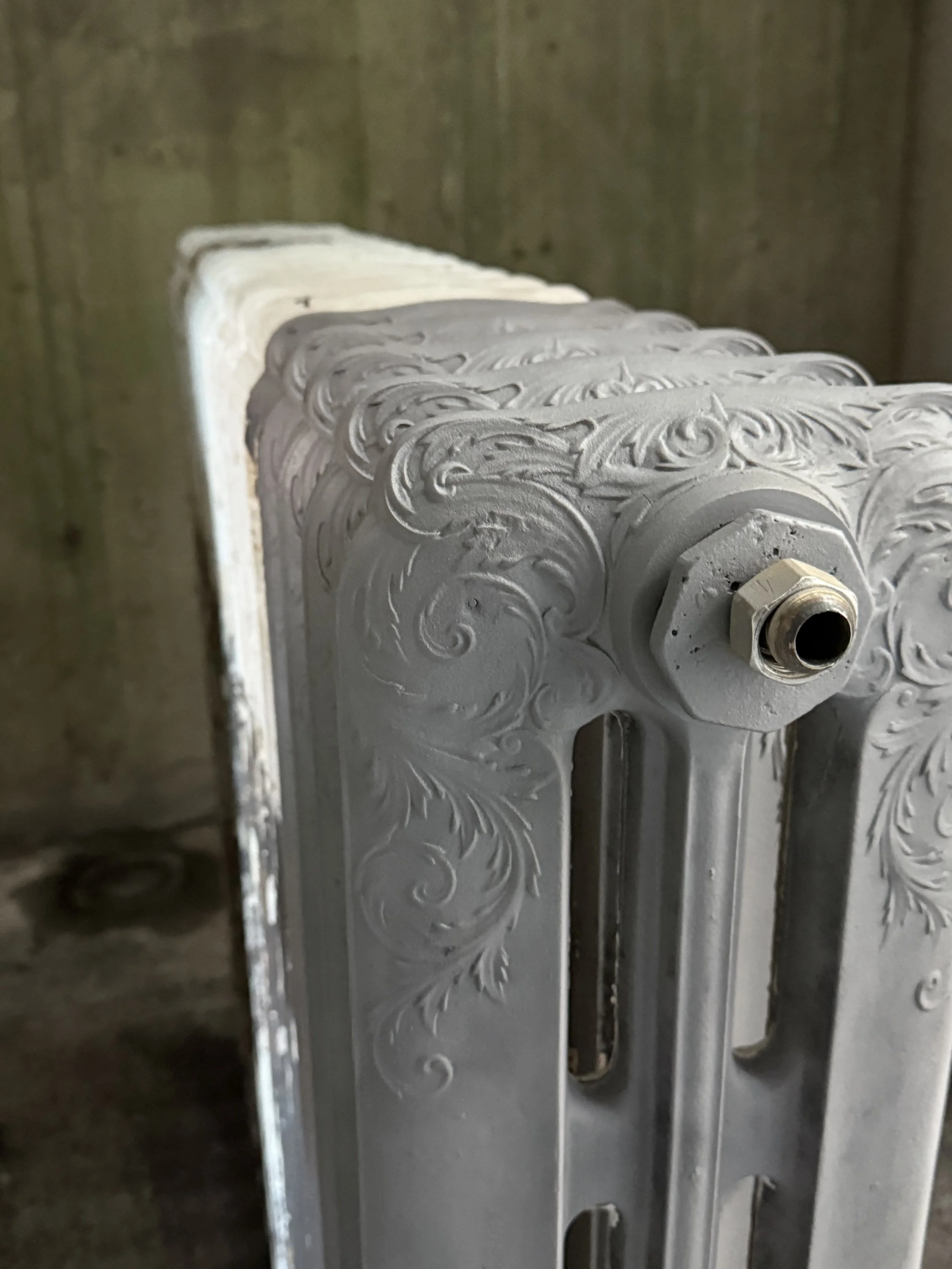 Ein antiker Messing-Heizkörper mit aufwändigen Christl-Verzierungen, an einer Wand in einem rustikalen Raum.