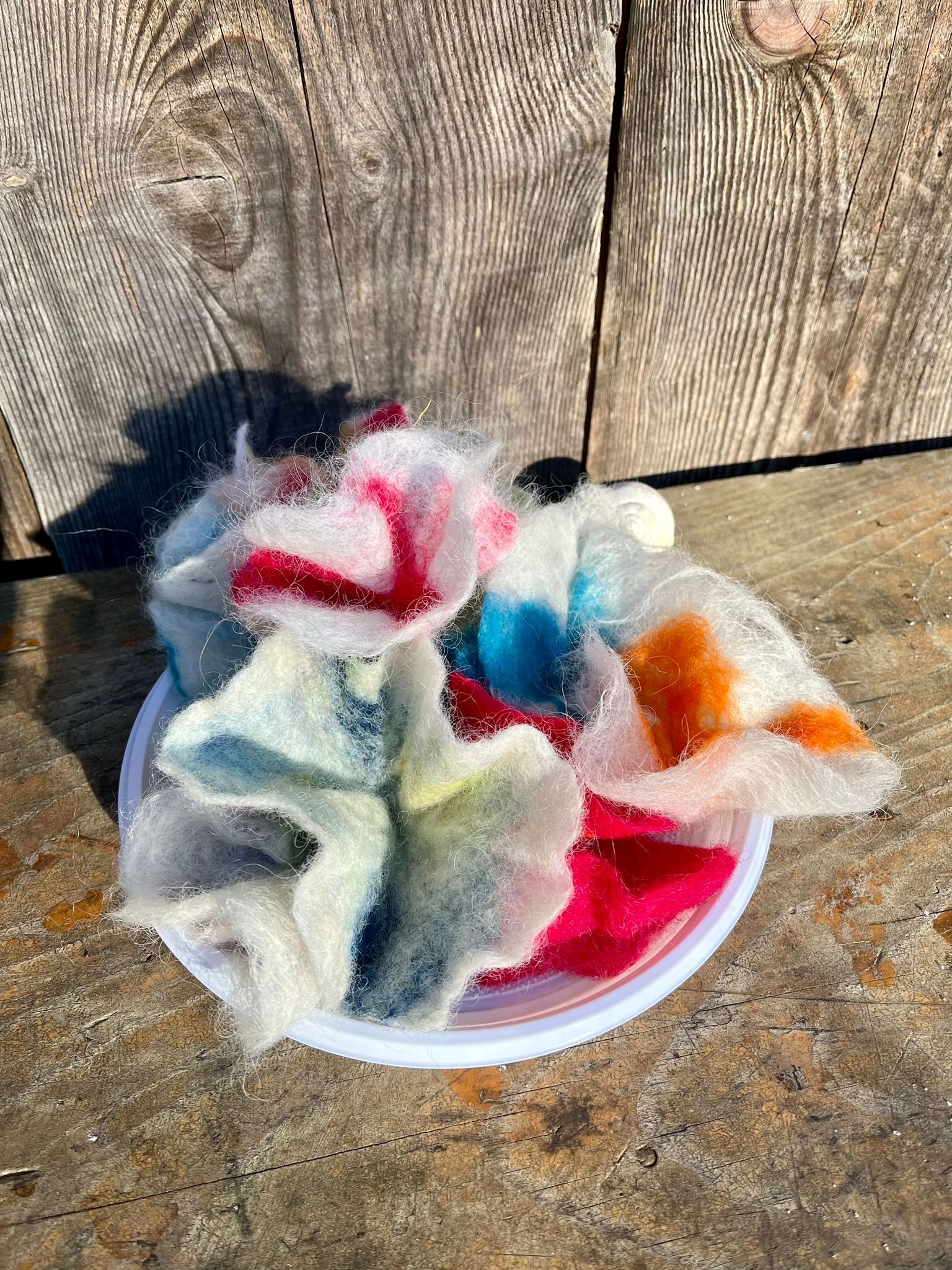 Gefilzte Wolle in verschiedenen Farben in einer Schale auf einem Holztisch.