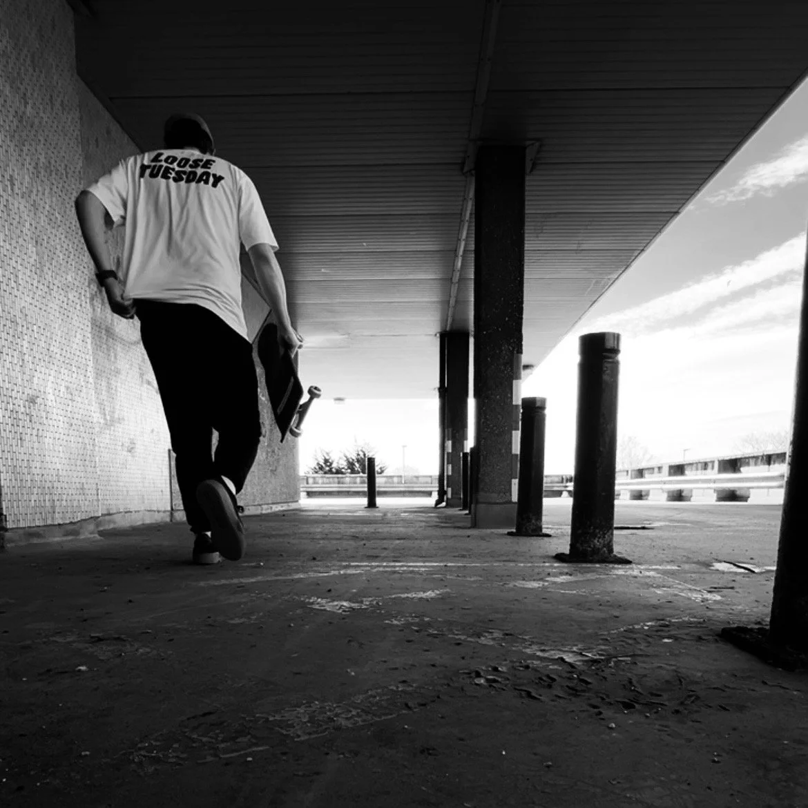 Black and white photograph of person wearing loose tuesday t-shirt against concrete walkway
