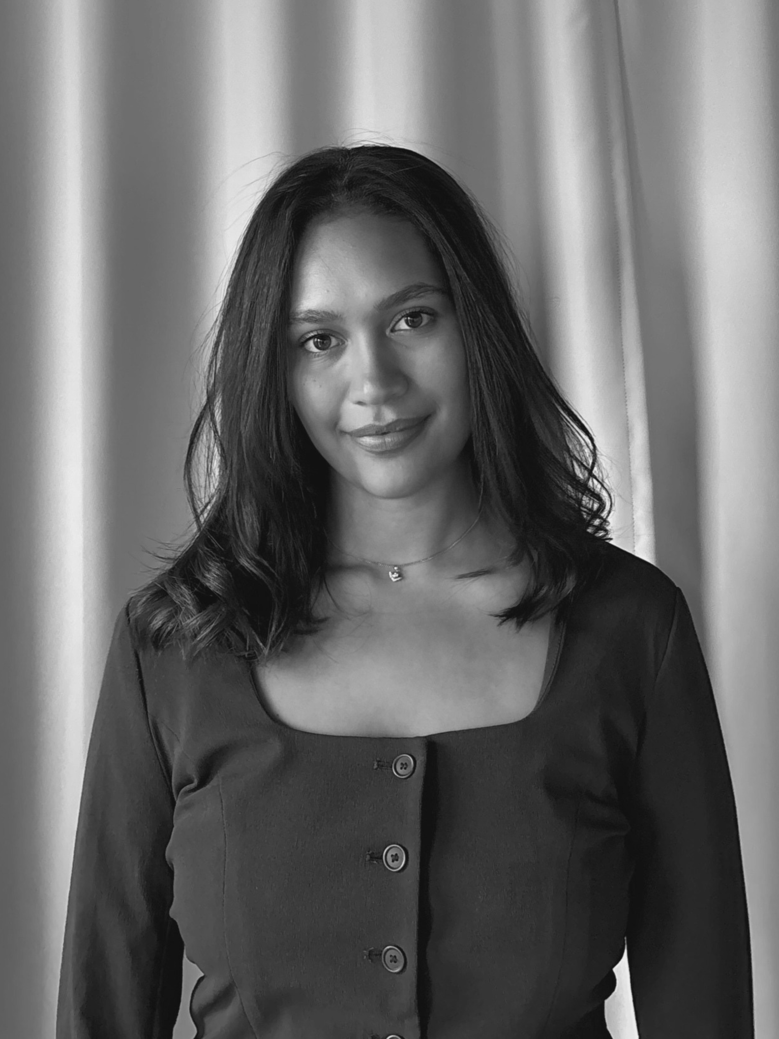 Black and white portrait of a young woman smiling, with shoulder-length hair, wearing a necklace and a casual T-shirt.
