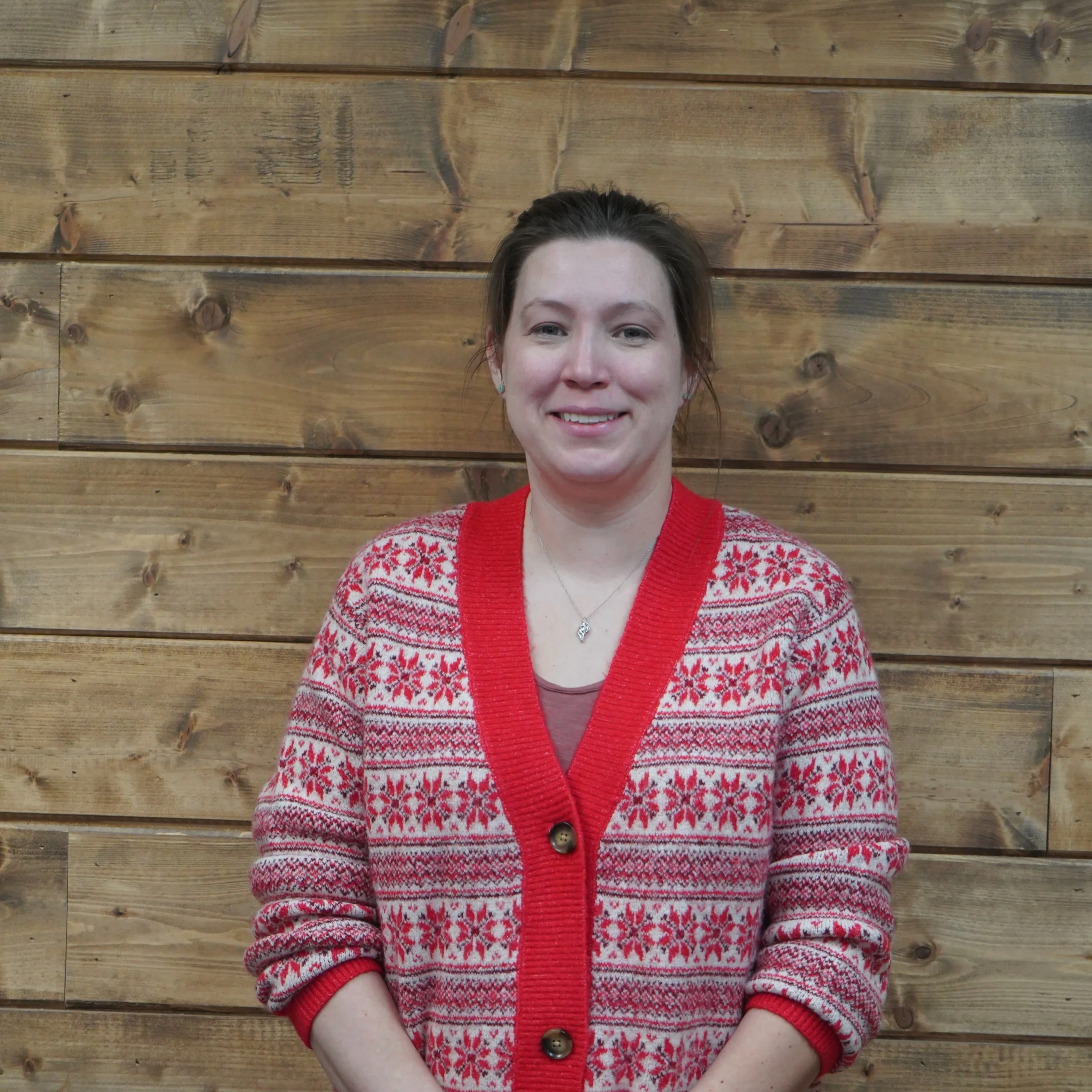 Woman standing in front of a wooden wall, wearing a festive red and white patterned sweater with a v-neck and buttons.