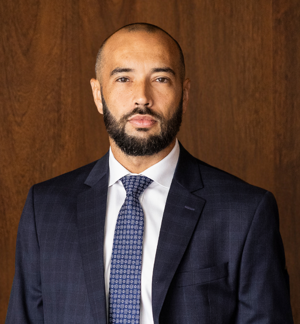 Man in business suit and tie standing in front of a wooden wall.