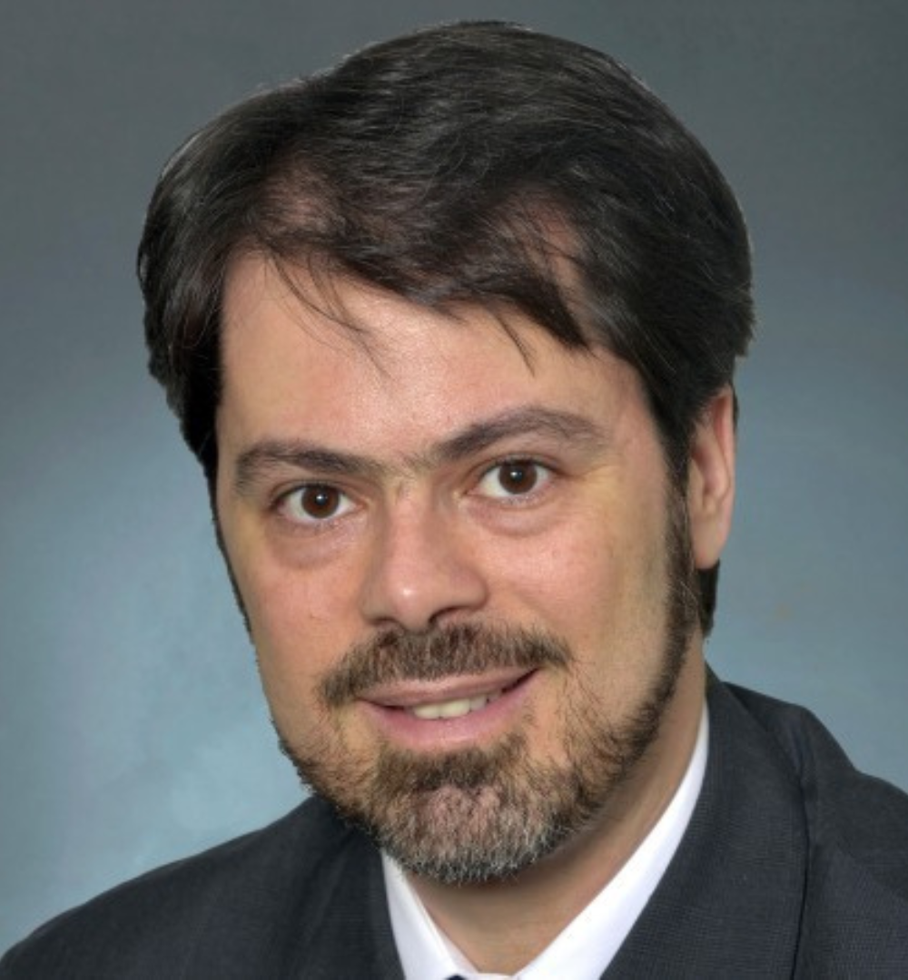 Portrait of a man with dark hair and a beard wearing a suit