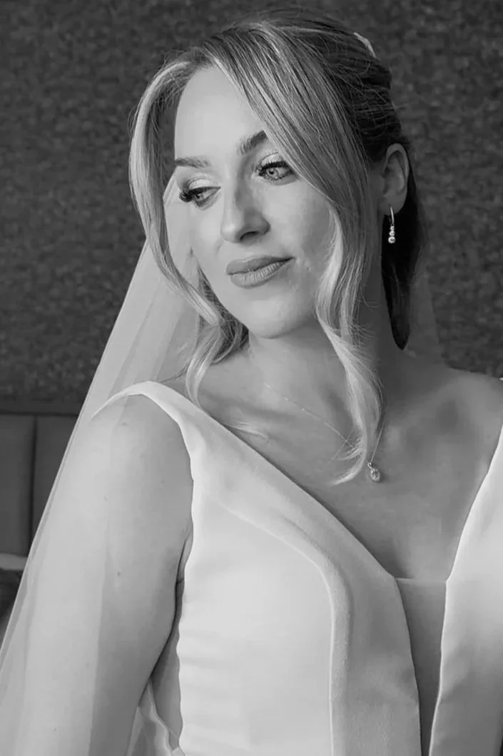 A black and white photo of a woman in a wedding dress with a veil, looking slightly to the side with a serene expression.
