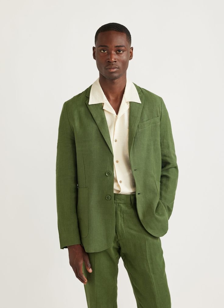 Man wearing a green suit with an off-white shirt, standing against a plain background.