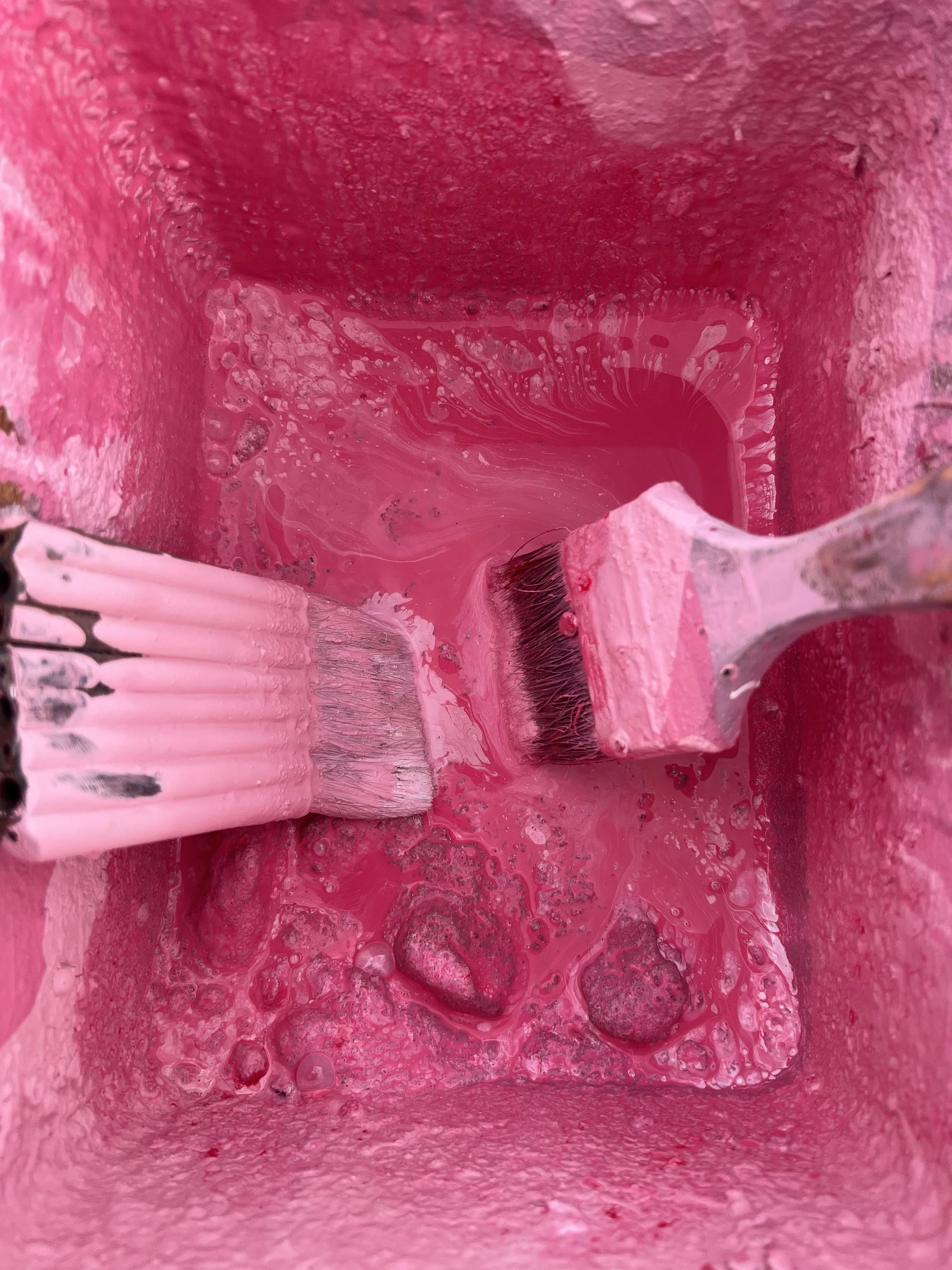 Close-up of a paintbrush applying bright pink paint to a textured surface.