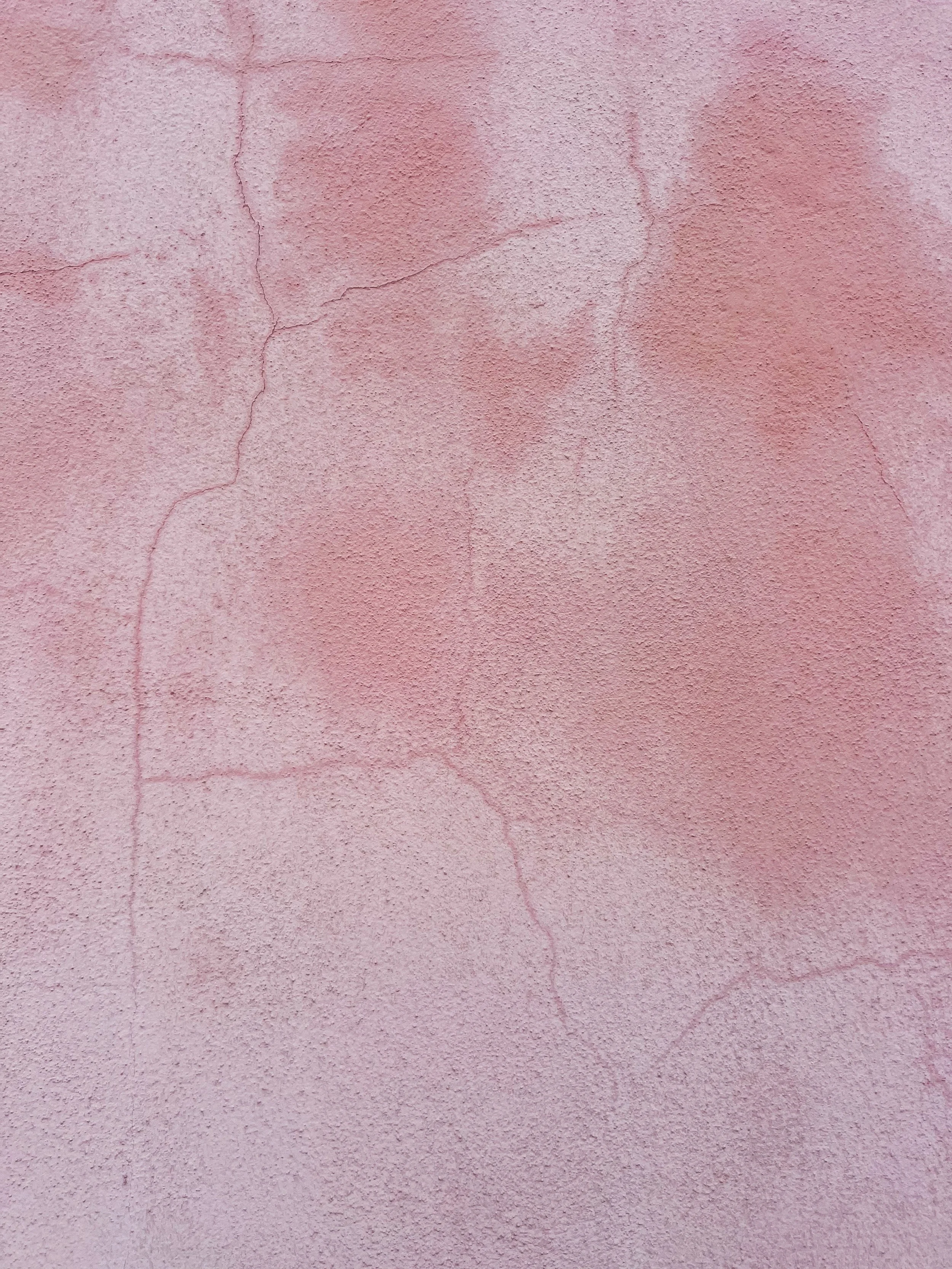 Close-up of a weathered pink stucco wall with visible cracks and textured surface
