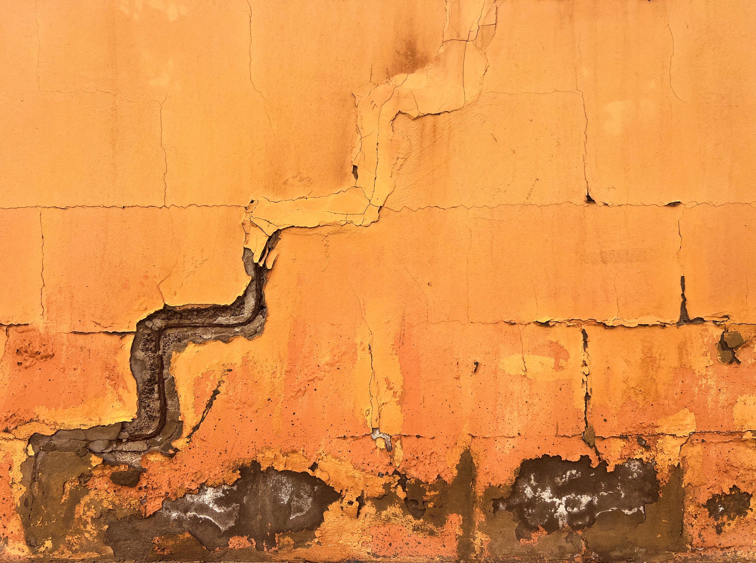 Close-up of a weathered orange wall with cracked, peeling plaster exposing dark masonry.