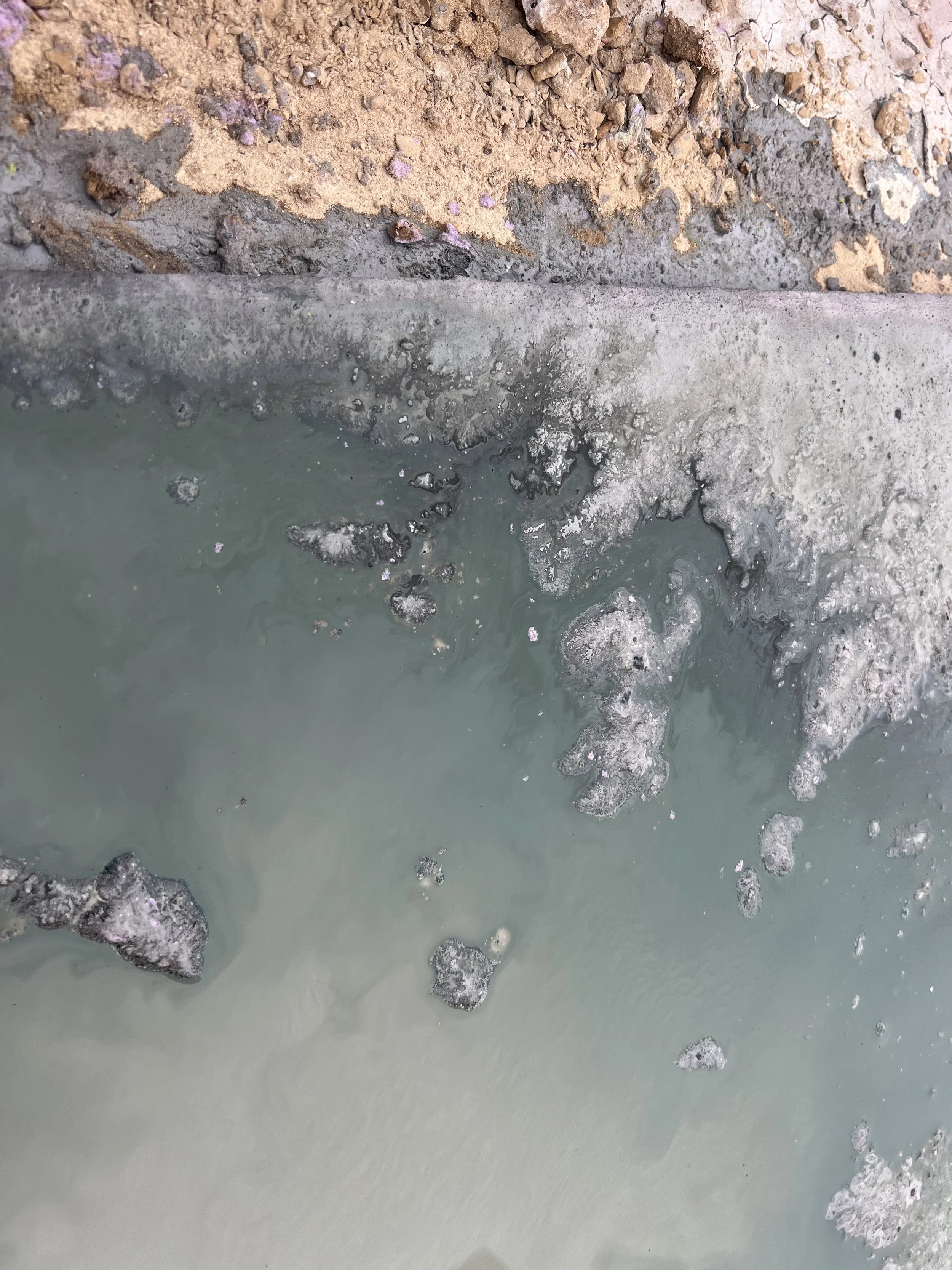 Close-up of murky water with scattered rocks and a crumbling, sediment-covered concrete edge