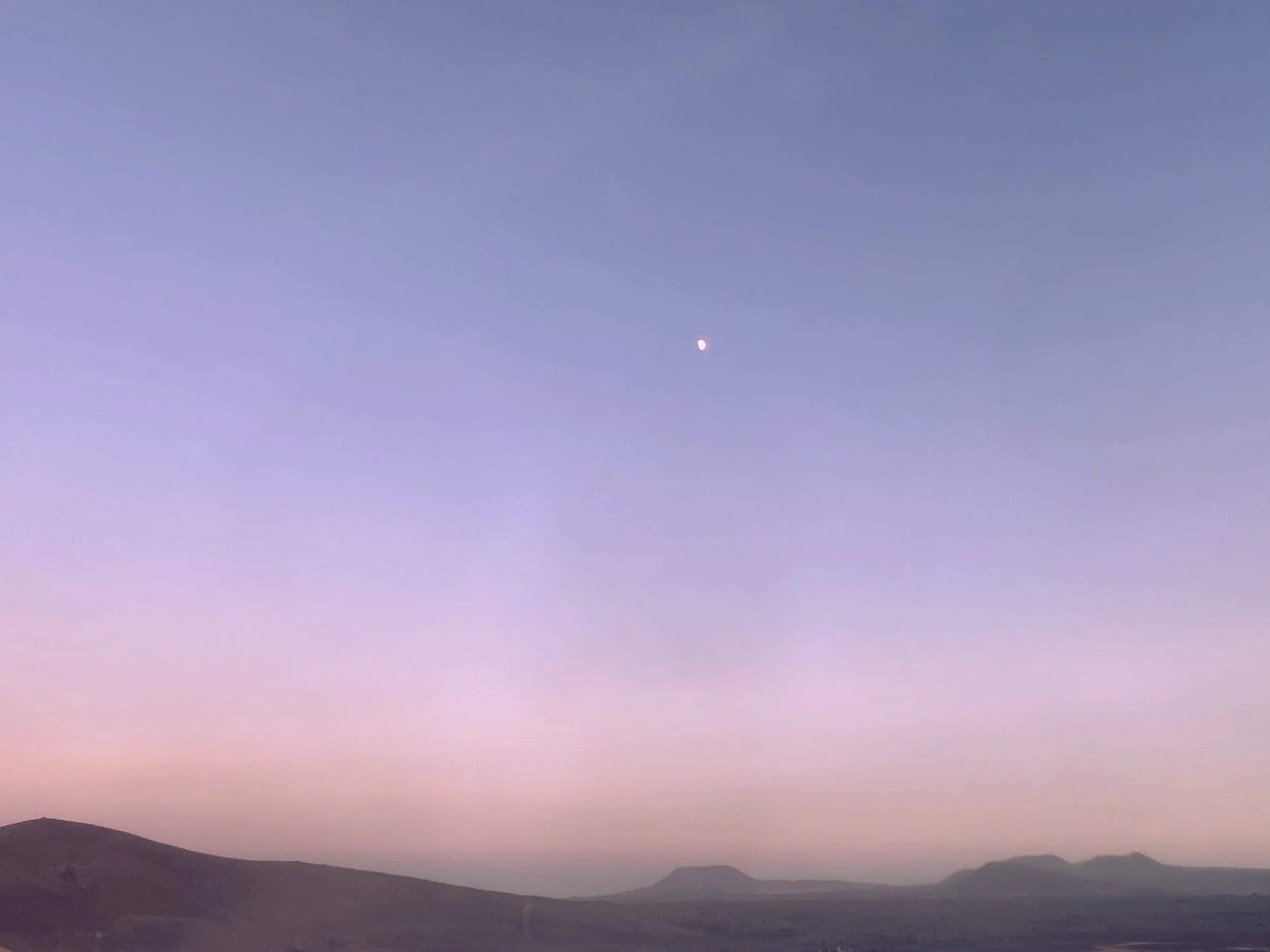 Dusk landscape with a crescent moon above silhouetted mountain ranges and a pink-purple sky