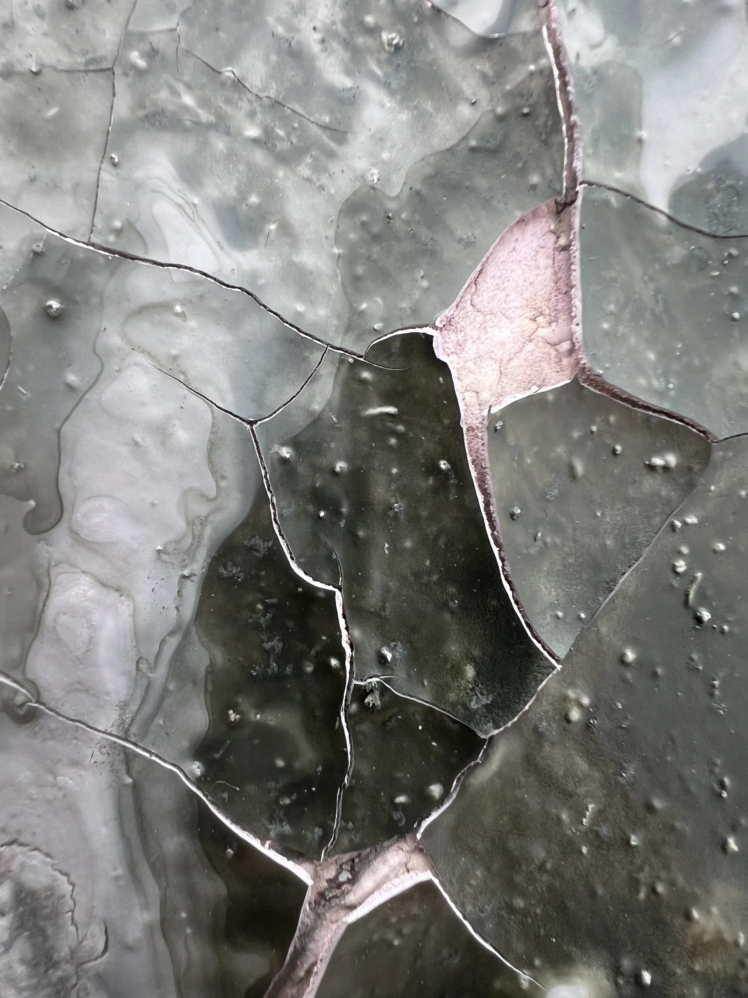 Close-up of cracked, weathered gray and pink glazed ceramic tiles with water droplets.