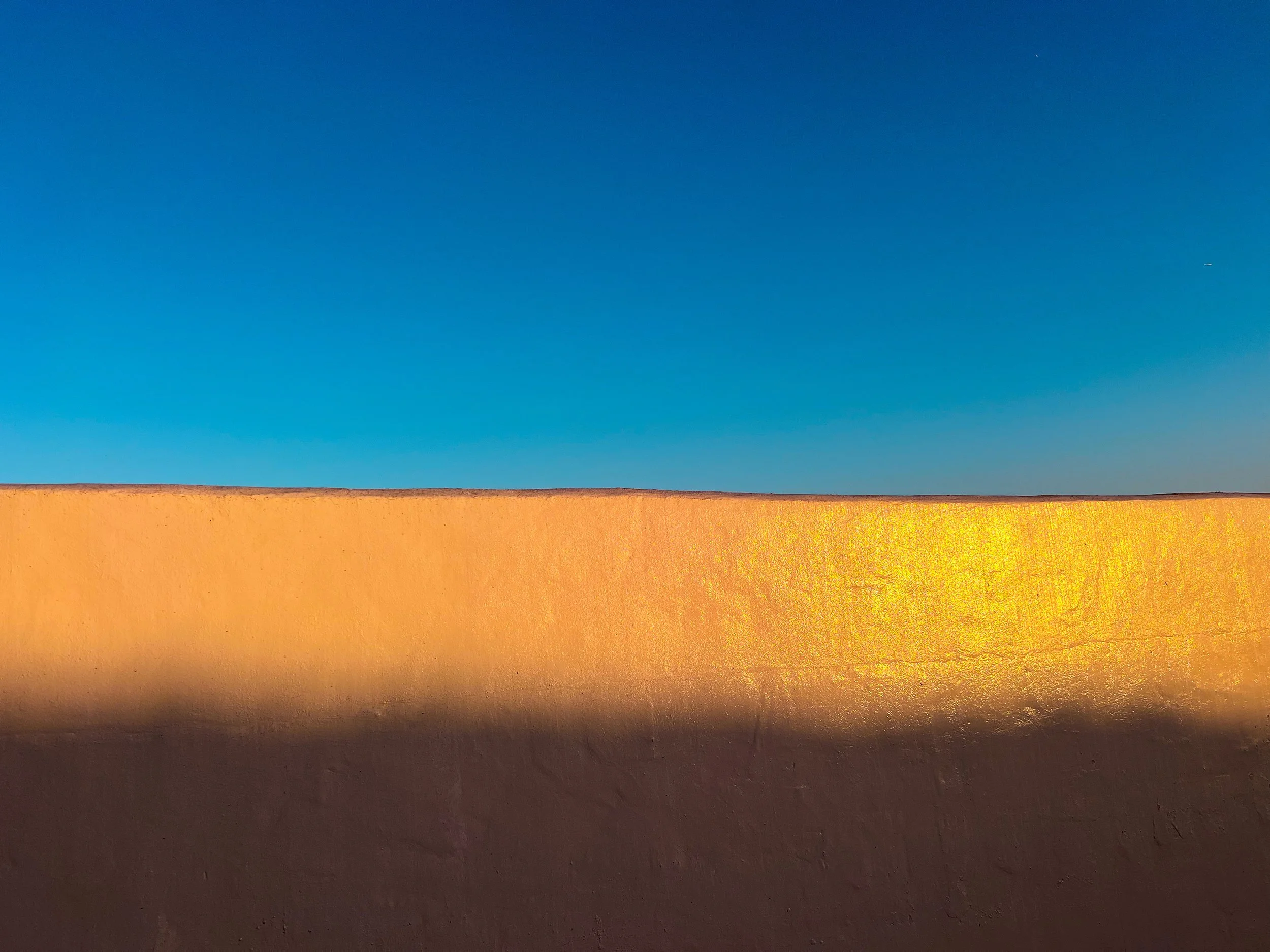Minimalist landscape with a blue sky above a sunlit golden desert horizon.