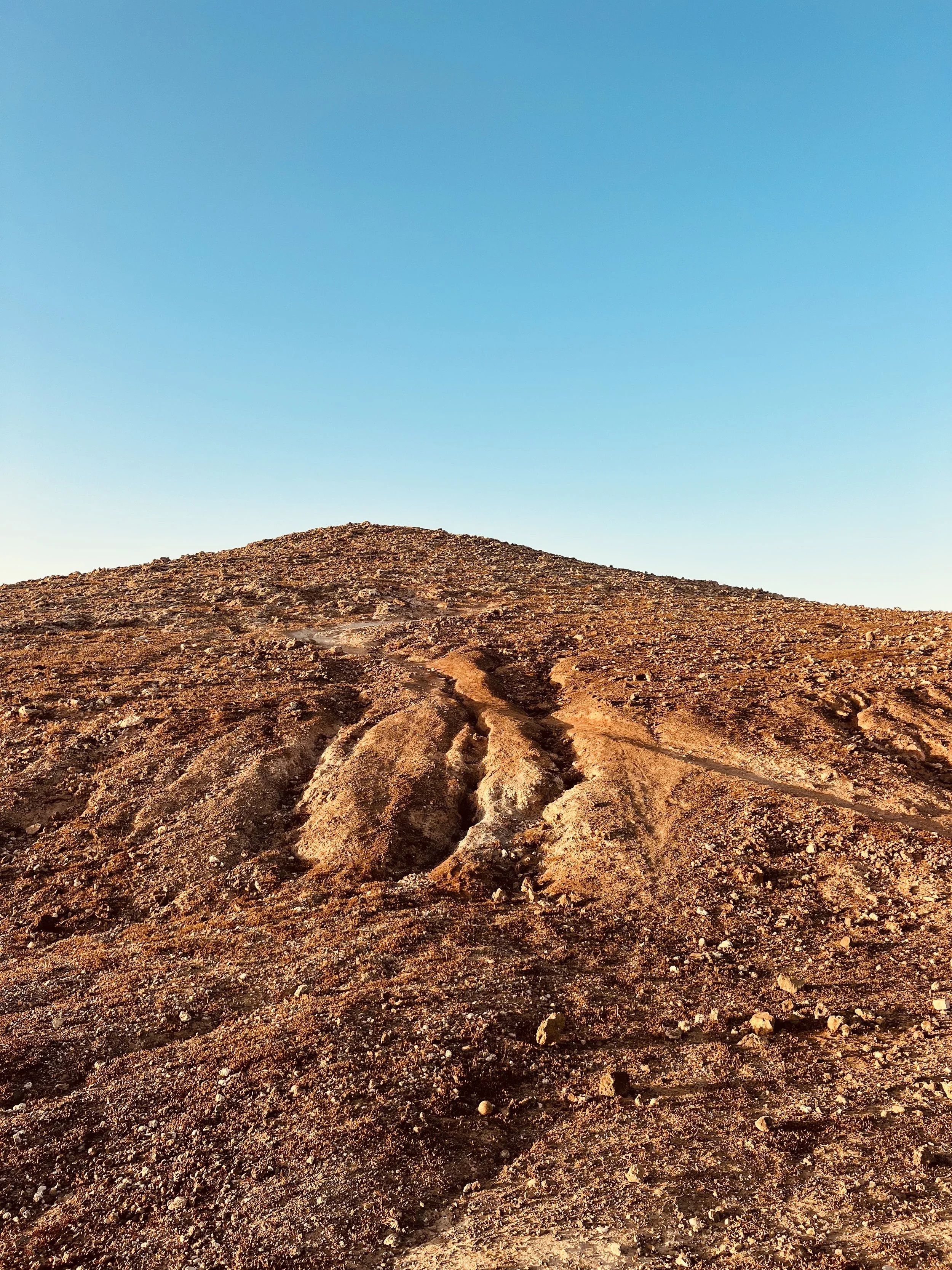 Barren rocky volcanic landscape with a rugged ridge beneath a clear blue sky