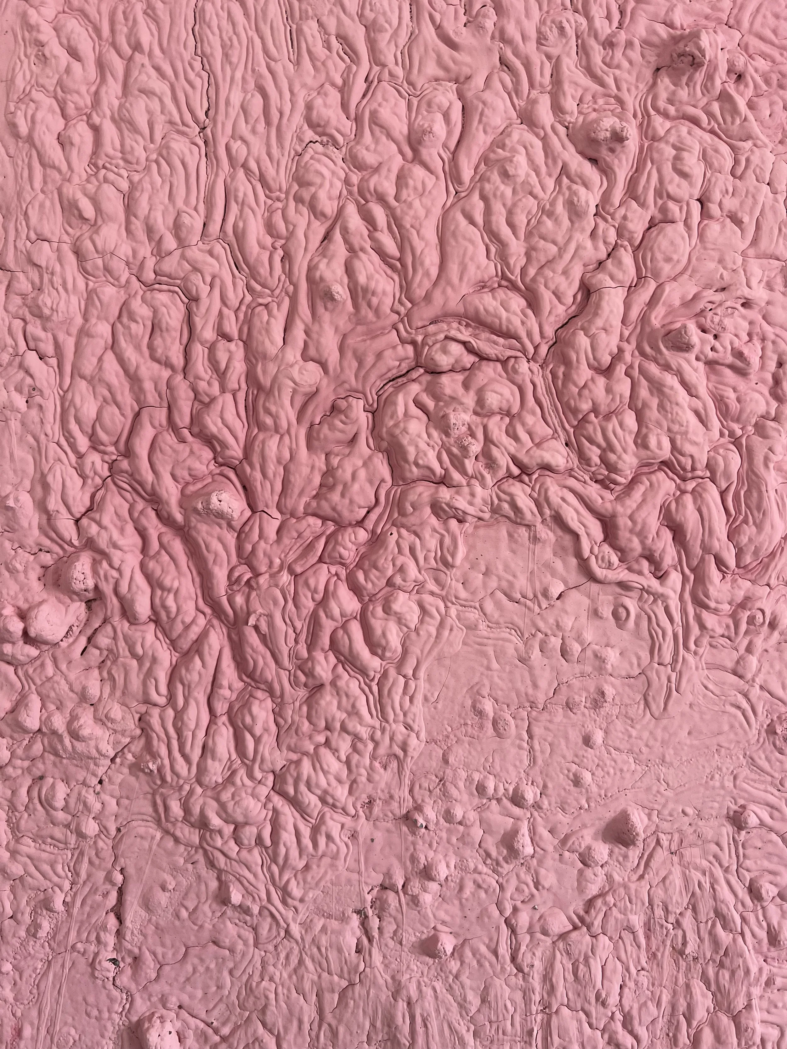 Close-up of pink textured plaster wall with raised, irregular patterns and cracks