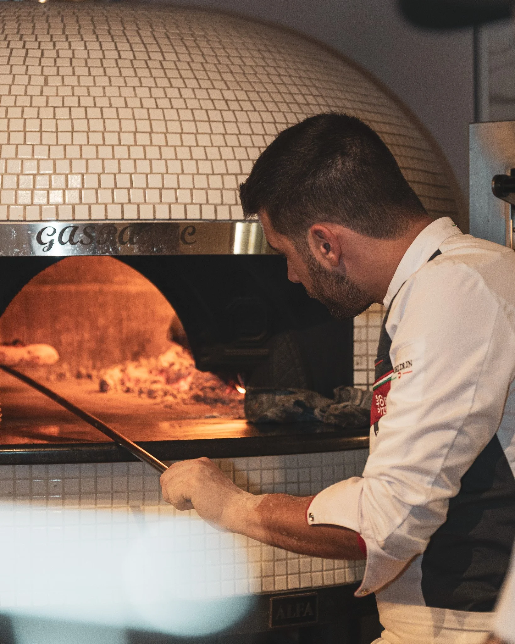 Un chef prepara una pizza en un horno de leña.