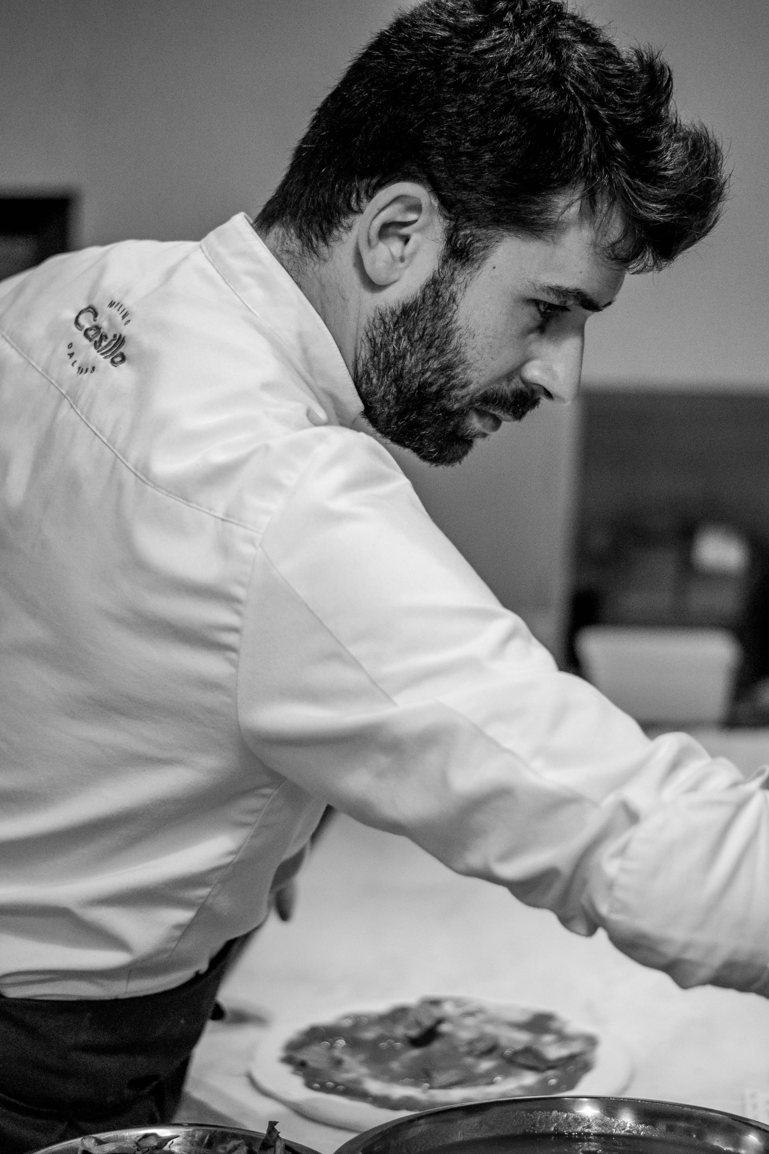 Eloi Torrent, vestido con chaqueta de chef, preparando una pizza en una cocina.