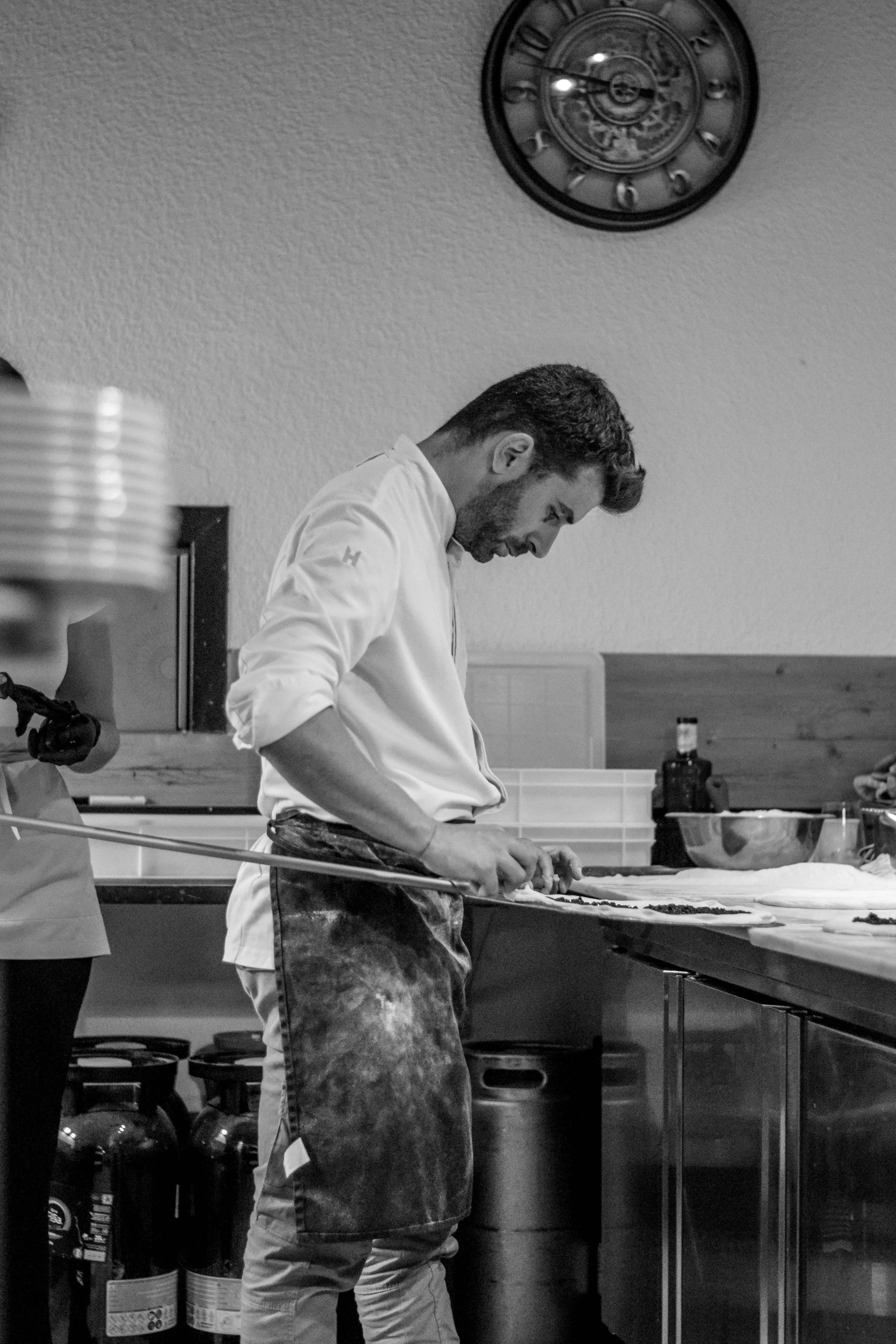Hombre cocinando en una cocina, vestido con pantalones manchados de harina o polvo, concentrado en preparar comida.