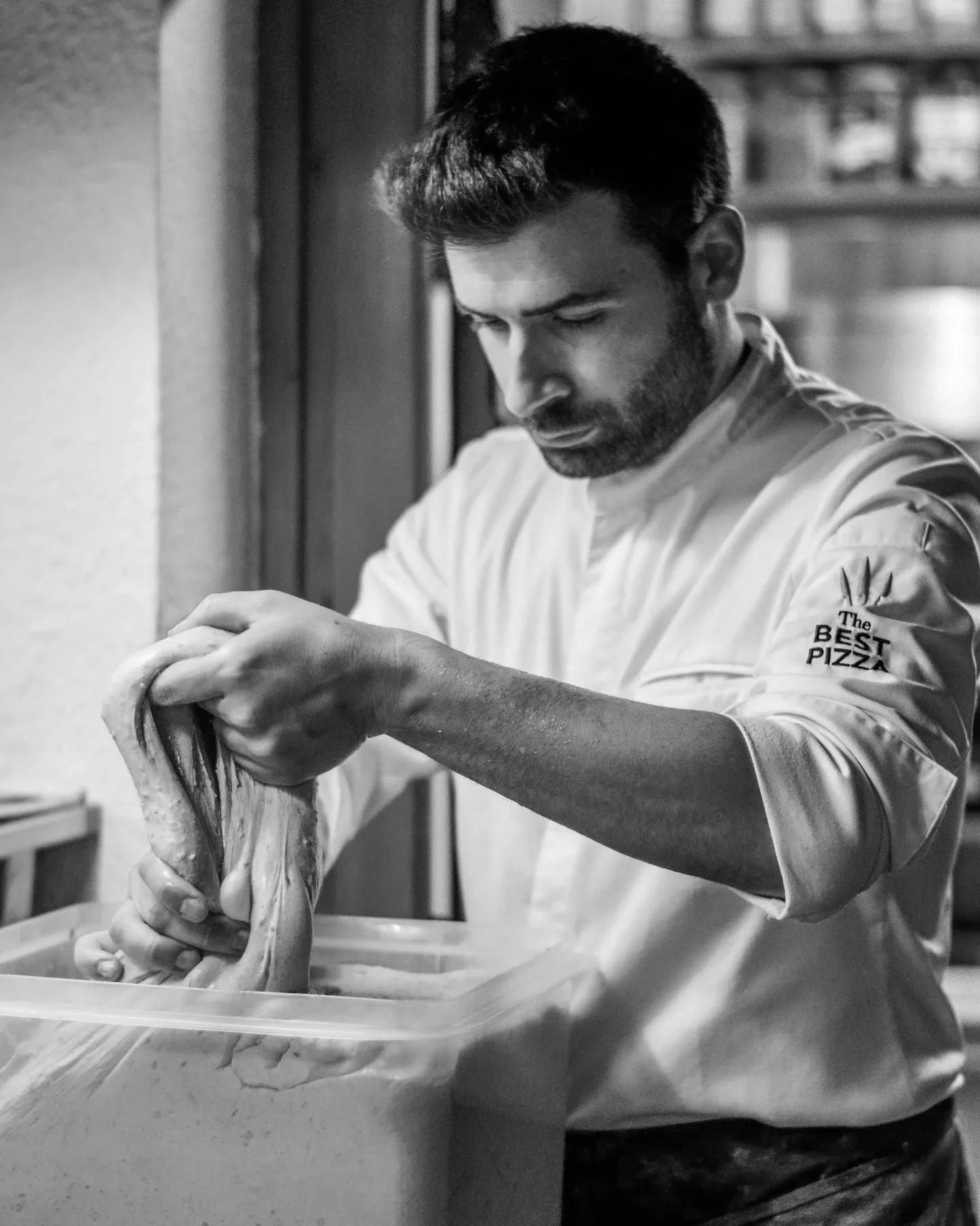 Hombre haciendo masa de pizza en una cocina, en blanco y negro.