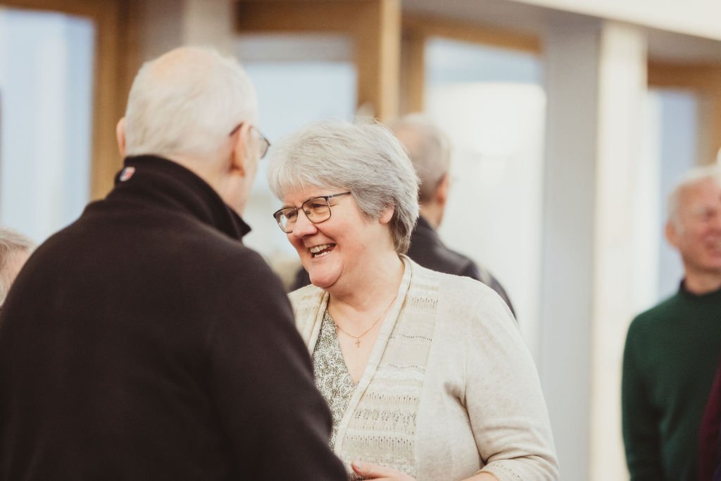 Smiling elderly woman and man talking at a social gathering.