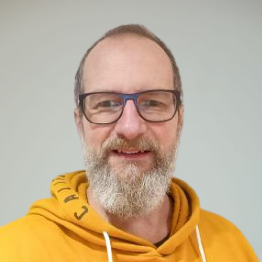 A man with glasses, a beard, and short hair wearing a yellow hoodie.