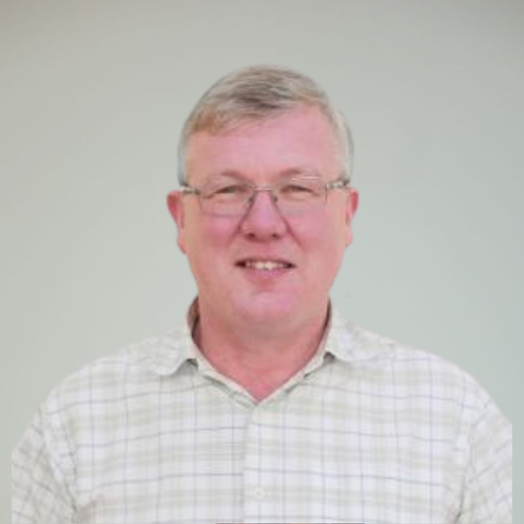 A man with light-colored hair, glasses, and a checkered shirt smiling at the camera against a plain, light-colored background.