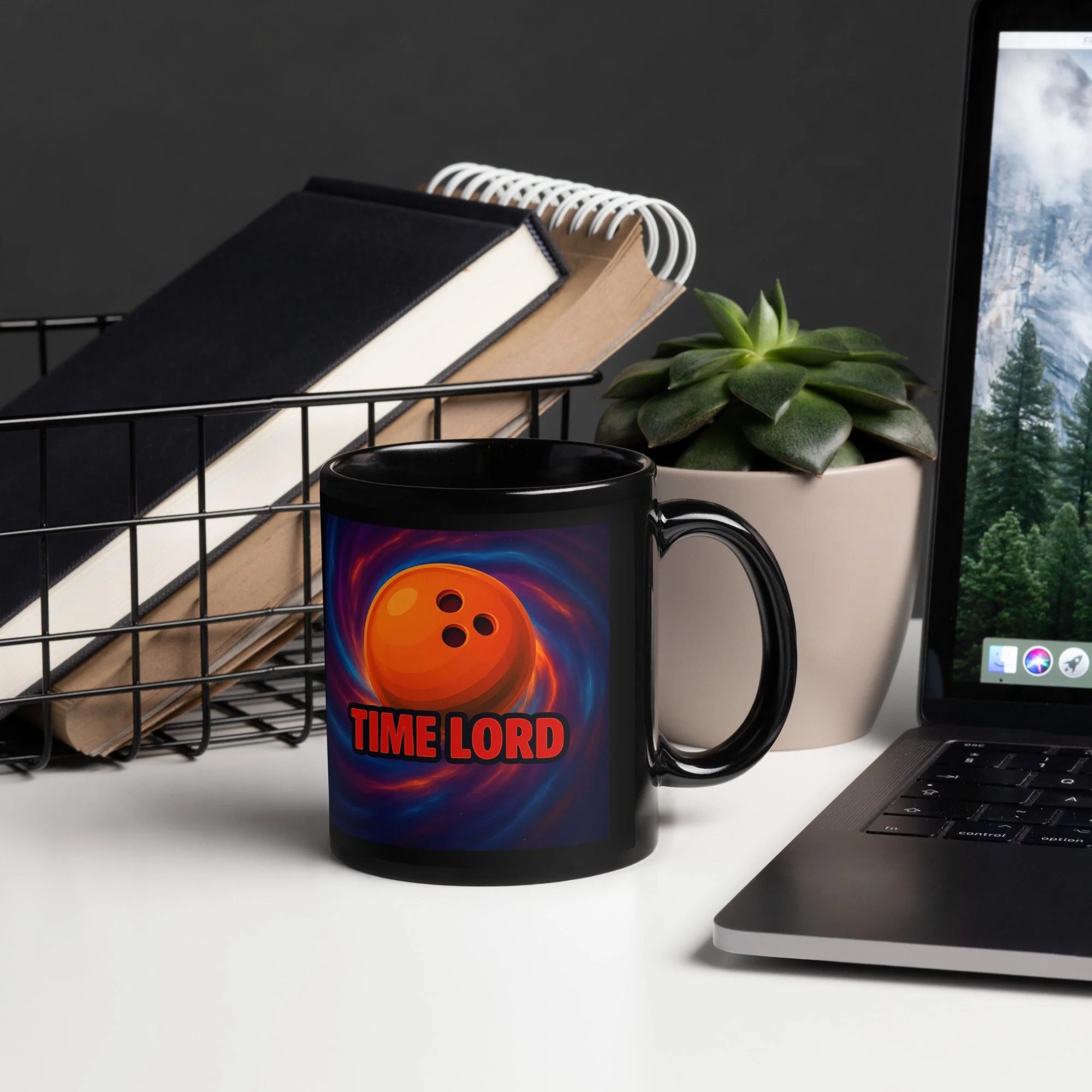 Black mug with a colorful swirling background, featuring an orange ball with black holes and the words "TIME LORD" in bold red letters, on a white desk alongside a laptop, a white plant pot with a succulent, and a black wire basket with notebooks.