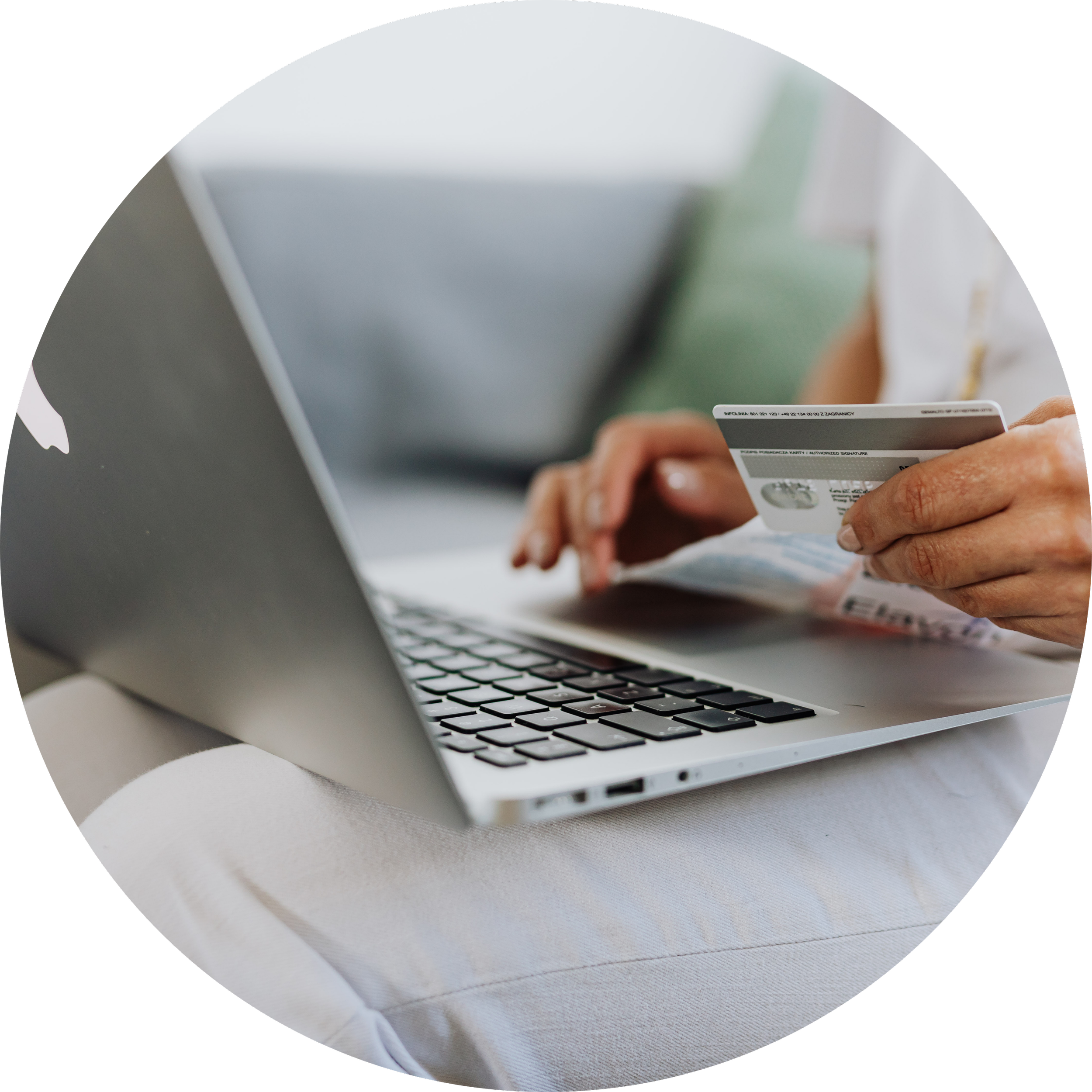 Close-up of a person holding a credit card and making an online purchase on a silver laptop, with a white table surface.