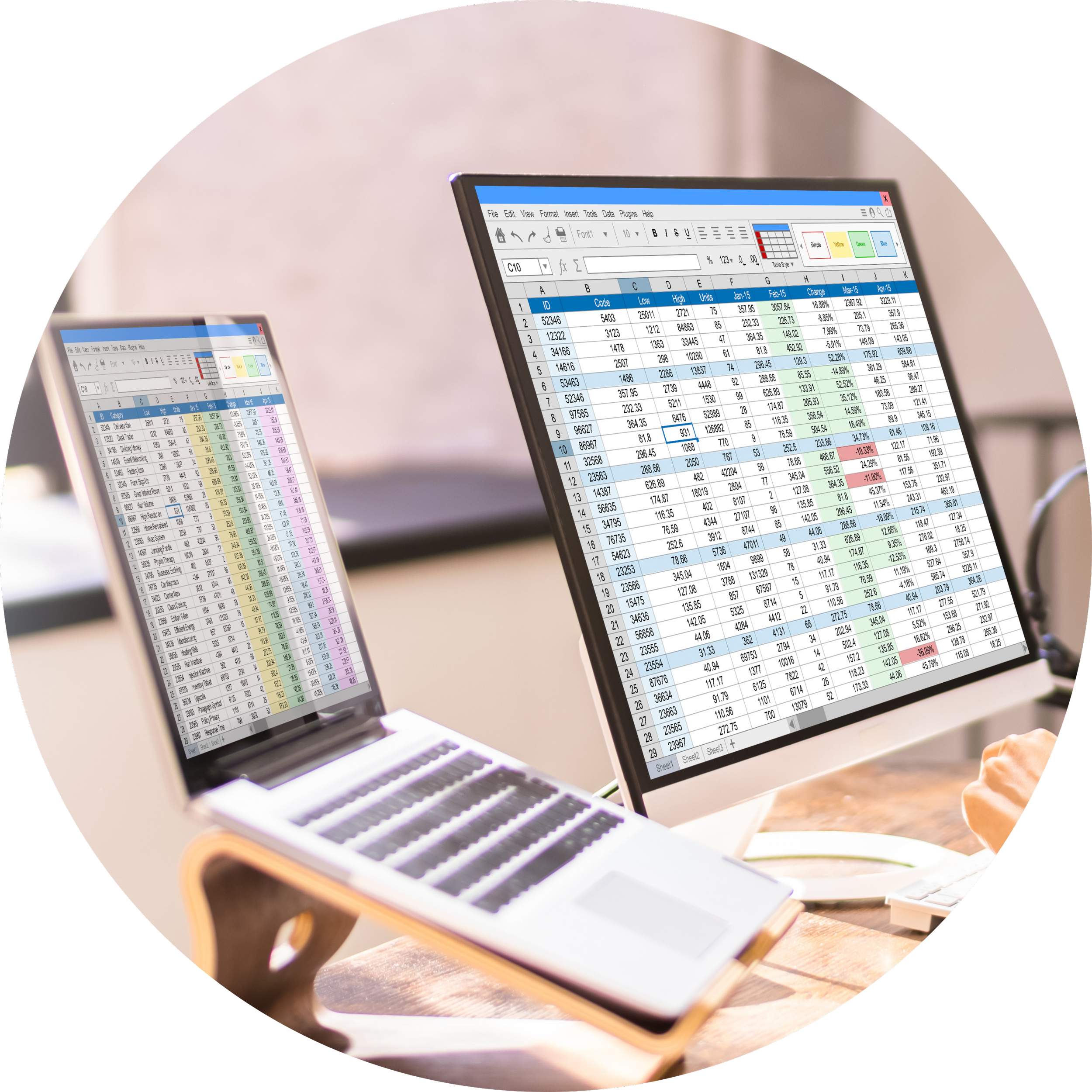 Two laptop screens displaying spreadsheets with financial data, one on a stand and the other on a desk.
