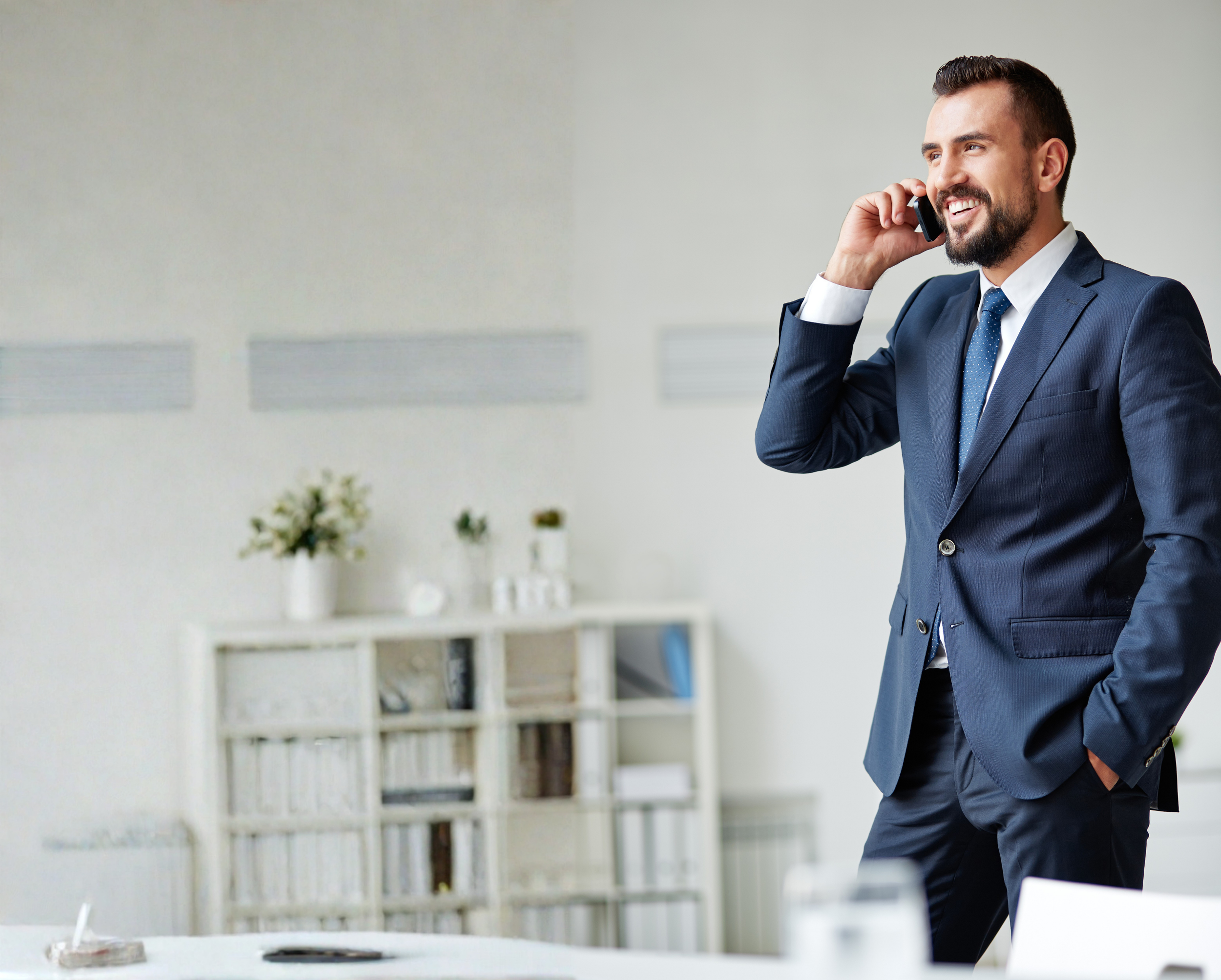 A man wearing a navy blue suit talking on a mobile phone in an office setting.