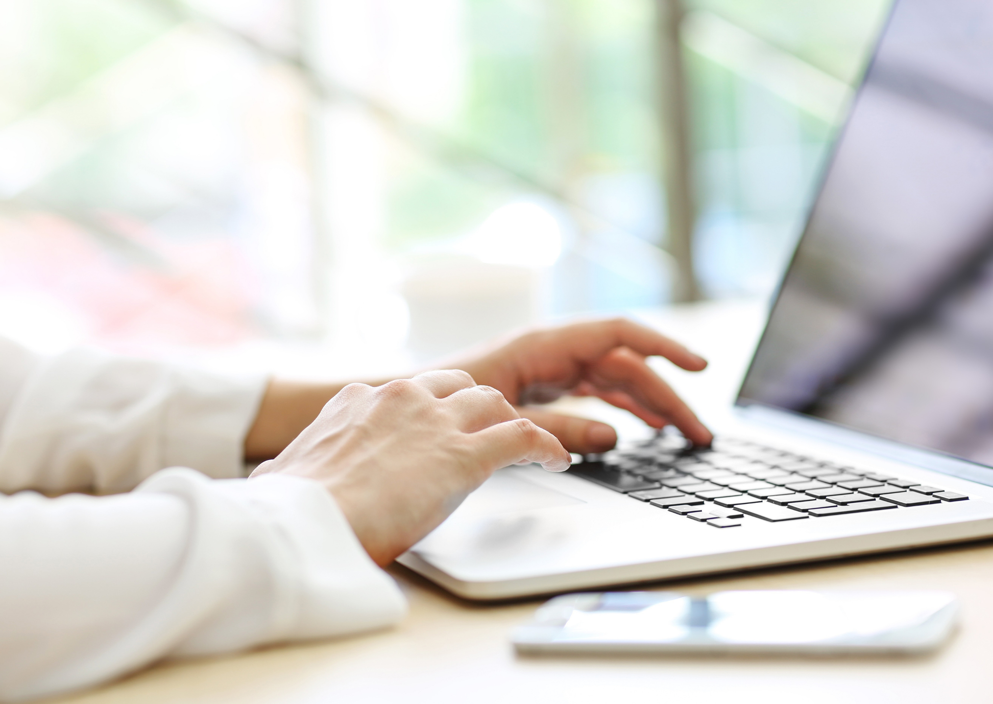 Close-up of person typing on a laptop keyboard with a blurred background.