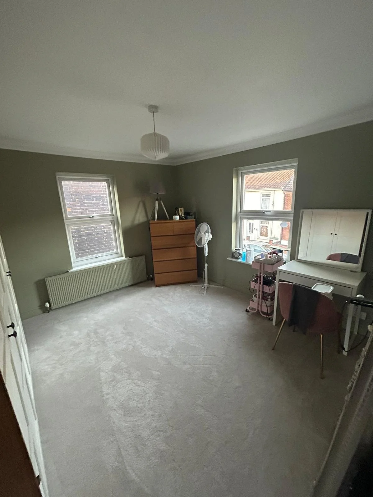 Bedroom with green walls, two windows, dresser, fan, desk with chair, and hanging light fixture.