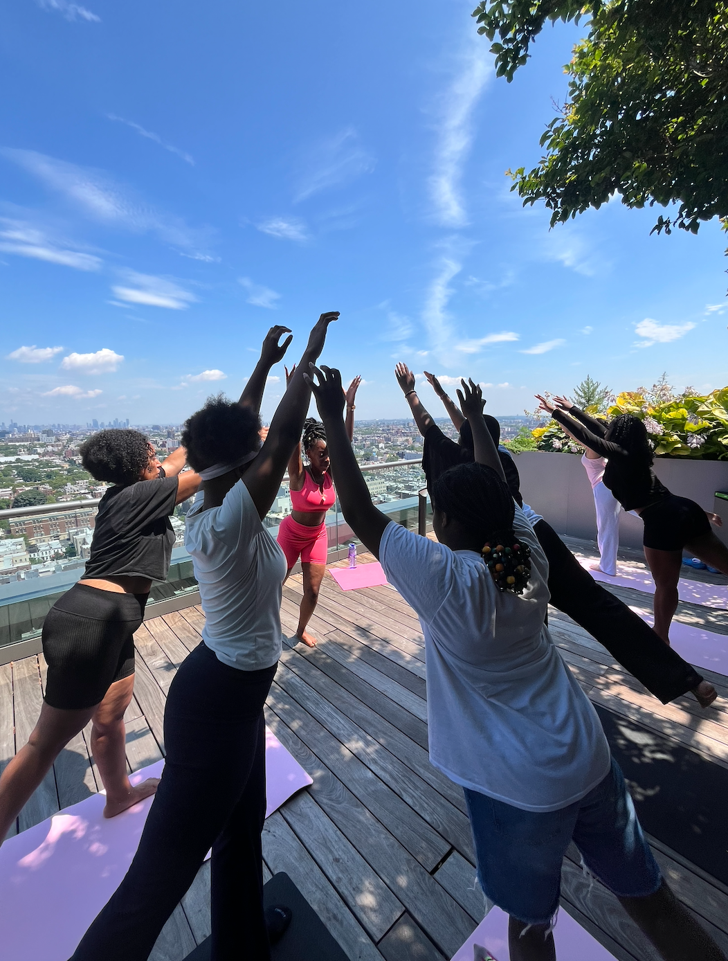 Group of people practicing yoga on a rooftop terrace under a blue sky with cityscape in the background.