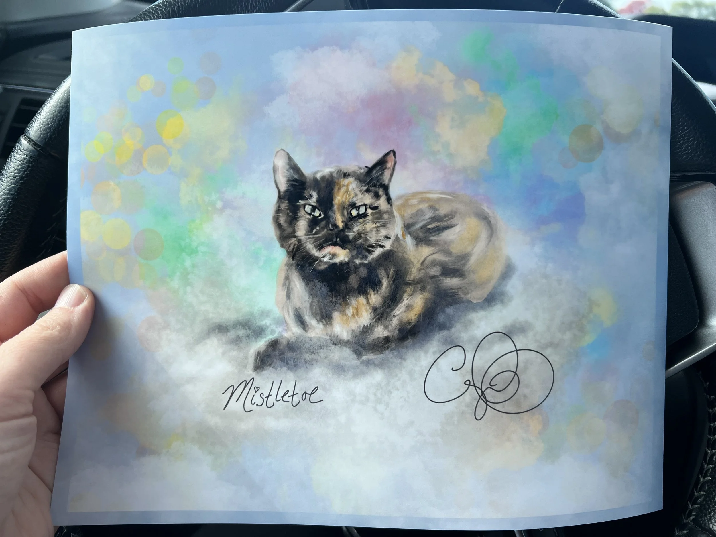 A colorful drawing of a calico cat with a mix of black, orange, and white fur, lying on a pastel-colored background with abstract circles and shapes, with the handwritten words 'Mistletoe' and 'E...'
