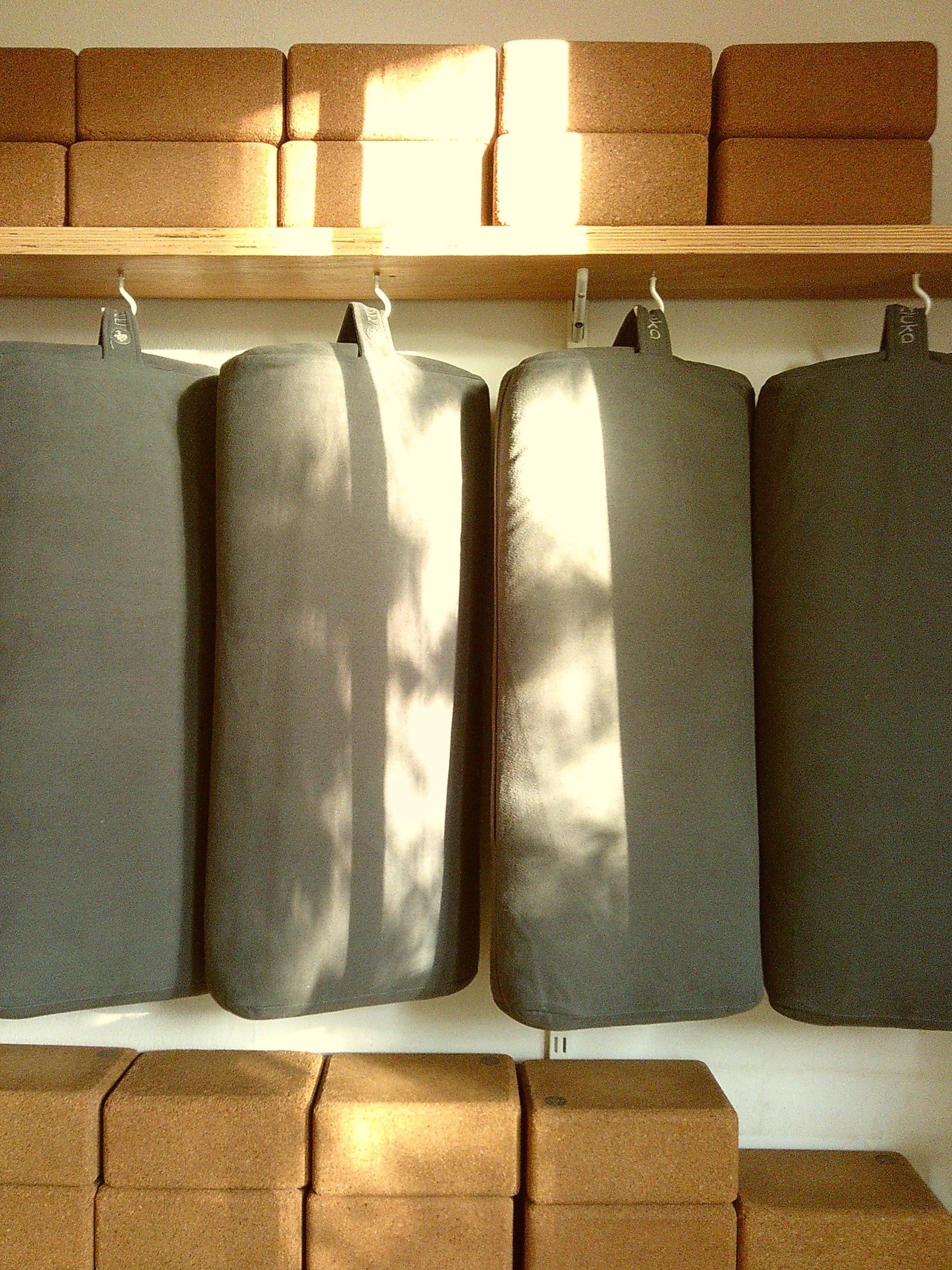 A display of three foam yoga blocks hanging on hooks on a wall, with a shelf of bricks above and more bricks below.