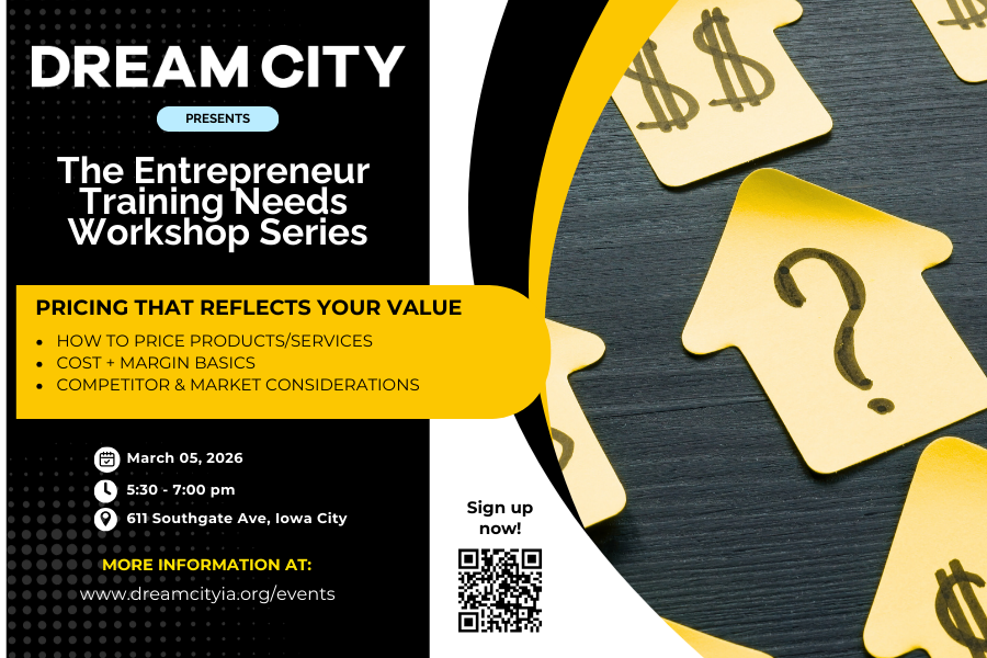 People attending a presentation in a bright, modern room with large windows, sitting at round tables covered with black tablecloths, listening to a speaker at the front.