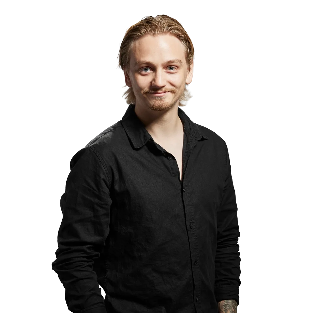 Porträtt av en man med ljusblont hår, skägg och mustasch, klädd i svart skjorta, mot en ljusgrå bakgrund.