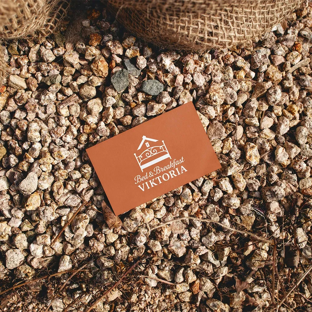 En klädd badge med texten "Bed & Breakfast VIKTORIA" ligger på grus med en söt randig korg ovanför.