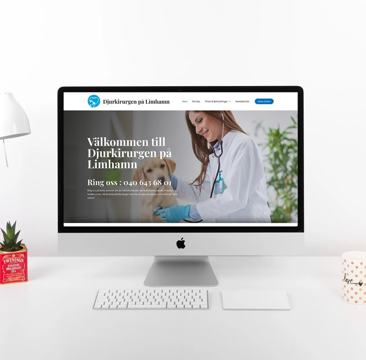 En dator som visar en hemsida för en veterinärklinik på Limhamn, med en kvinna som undersöker en hund. Runt datorn finns en växt, ett te-paket och en mugg.
