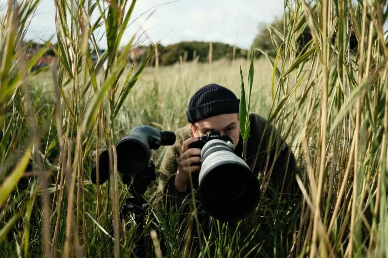 Person som fotograferar i ett fält med högt gräs.