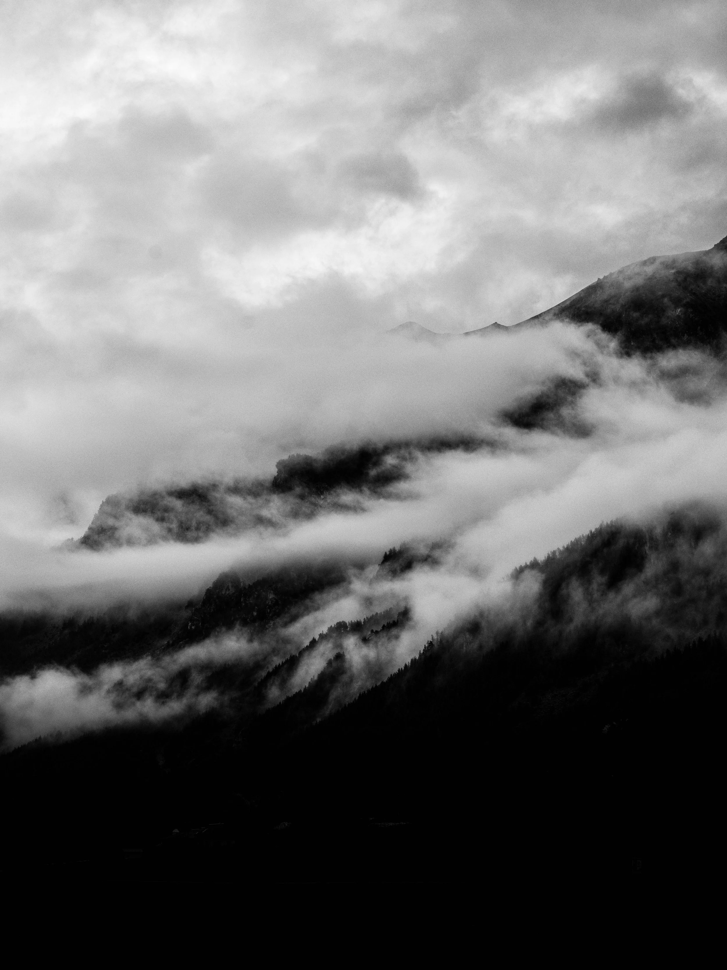 Black and white photograph of a mountain landscape with clouds and fog obscuring the peaks.